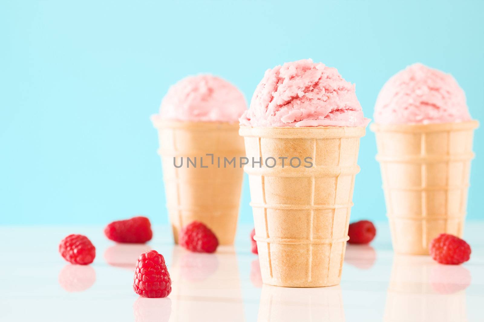 three raspberry ice cream cones with blue background