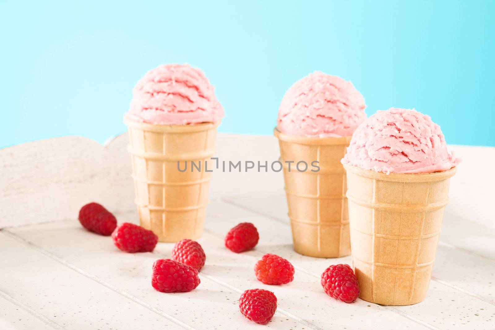 three raspberry ice cream waffle cones with raspberries on white wood