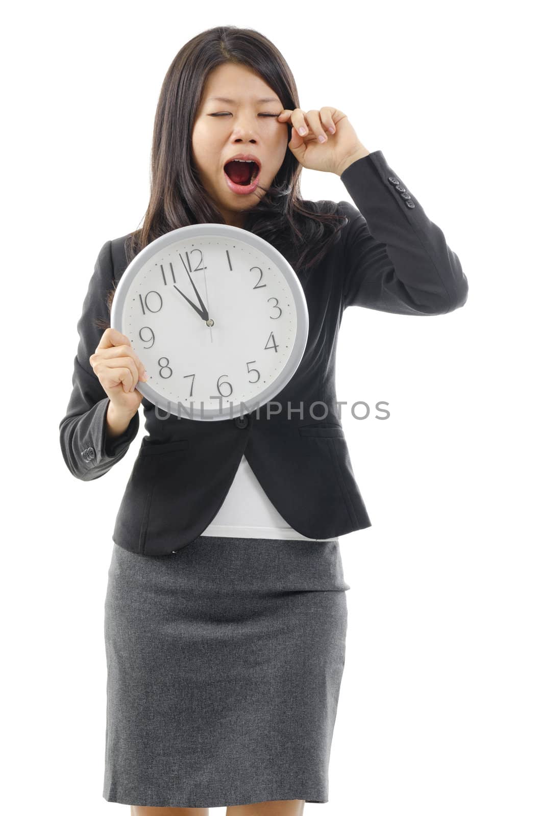 Tired Asian business woman holding a clock and rubbing eye, isolated on white background.