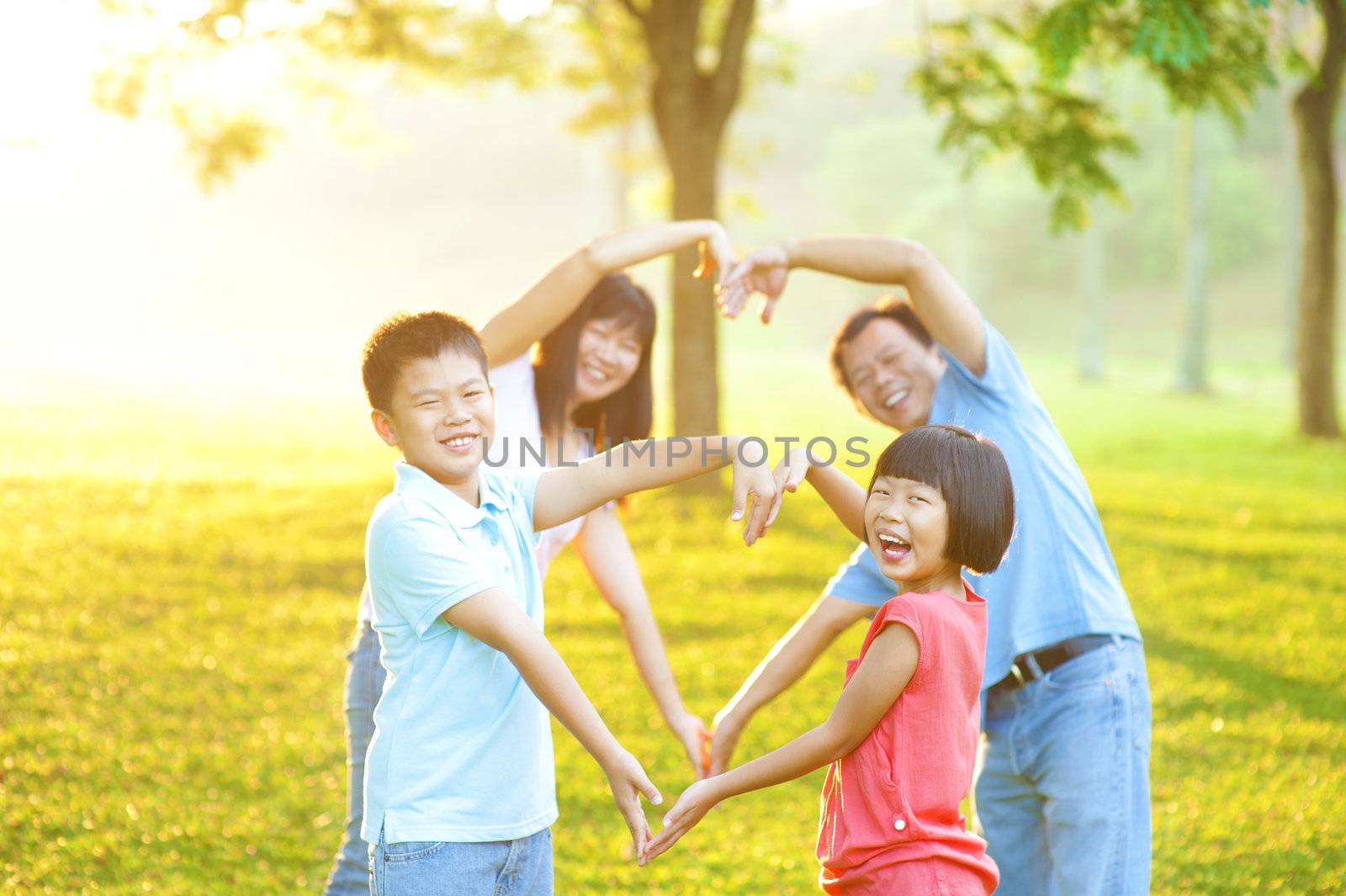 Happy playful Asian family forming love shape, outdoor green park