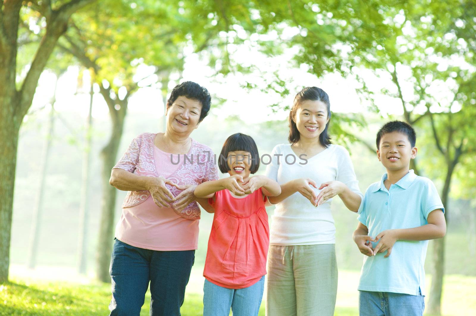 Happy playful Asian family forming love shape at outdoor green park