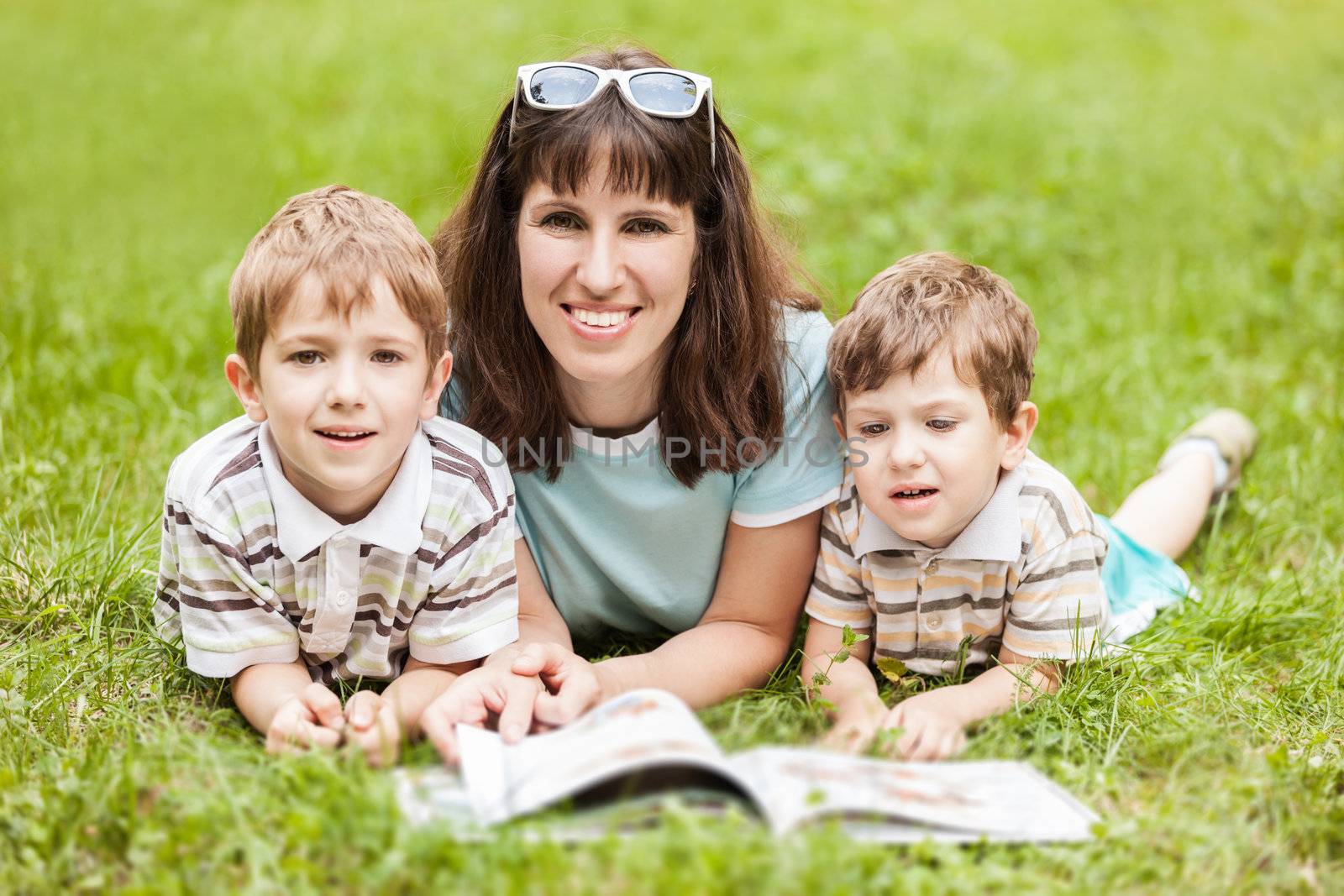 Mother and sons reading book outdoor by ia_64