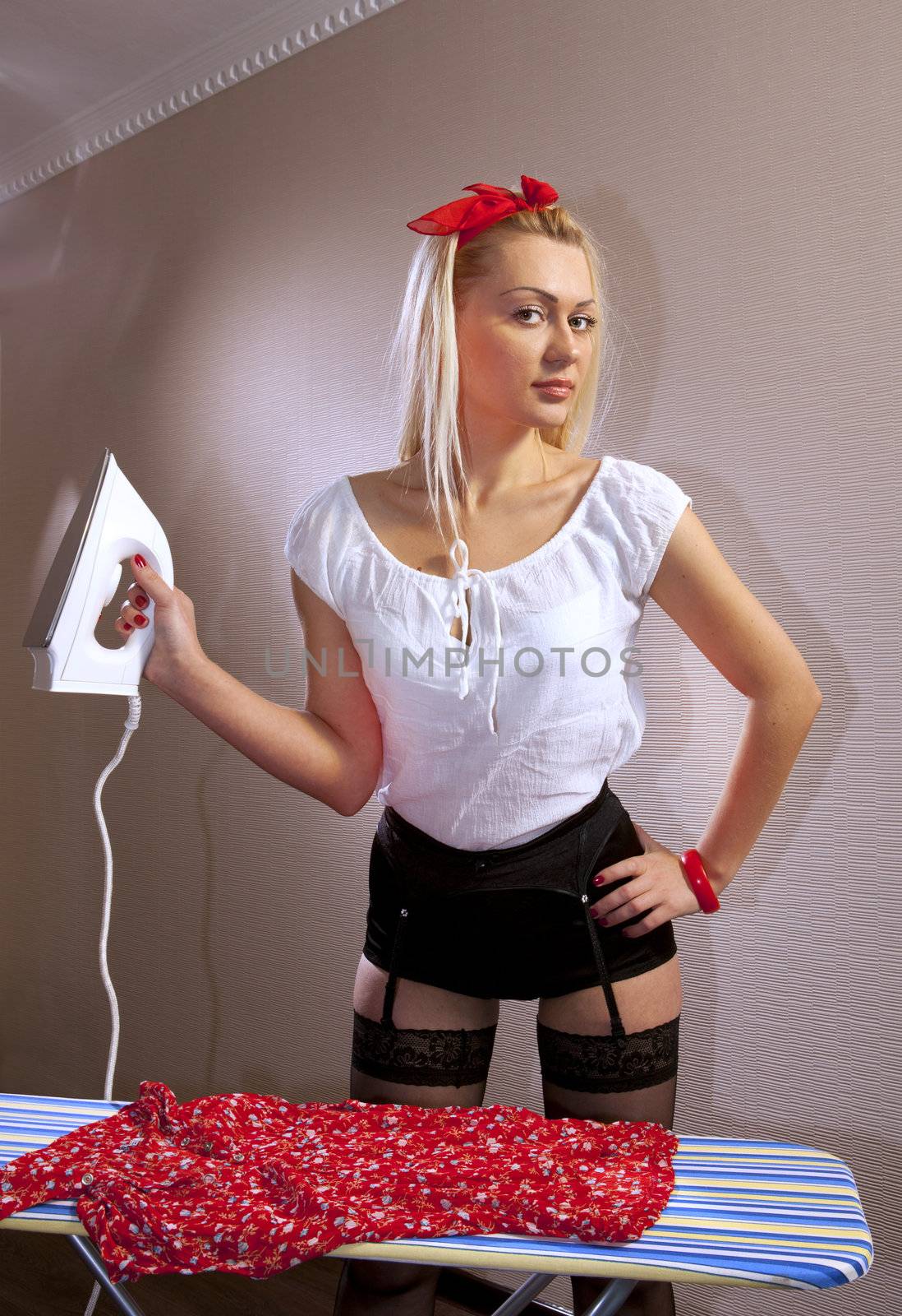 Beautiful housewife ironing a red blouse at home