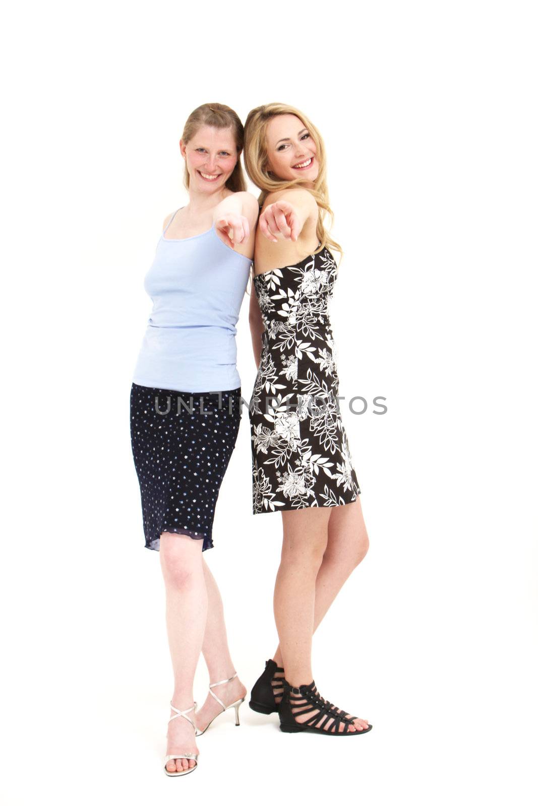 Two laughing attractive women standing back to back pointing with extended arms towards the camera isolated on white Laughing attractive women standing back to back pointing with extended arms towards the camera isolated on white 