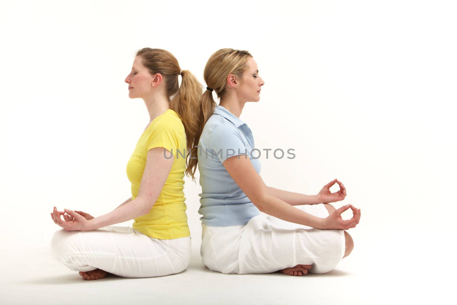 Two attracive female friends sitting back to back in the lotus position meditating together with peaceful expressions and their eyes closed 