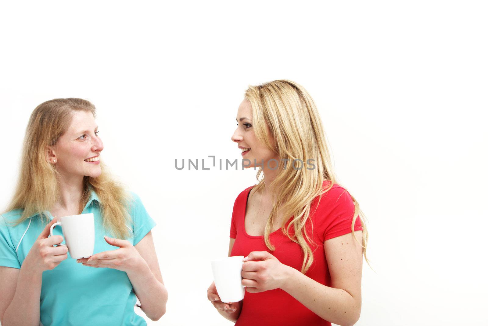 Two attractive young women standing chatting over a cup of coffee isolated on white 