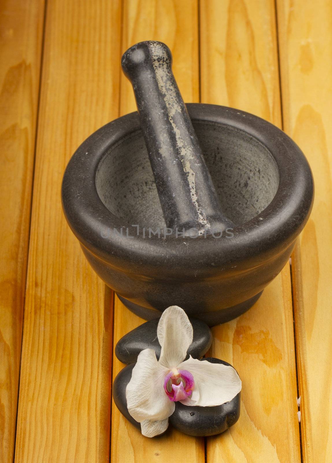 Mortar, pestle, orchid and stones over wooden background