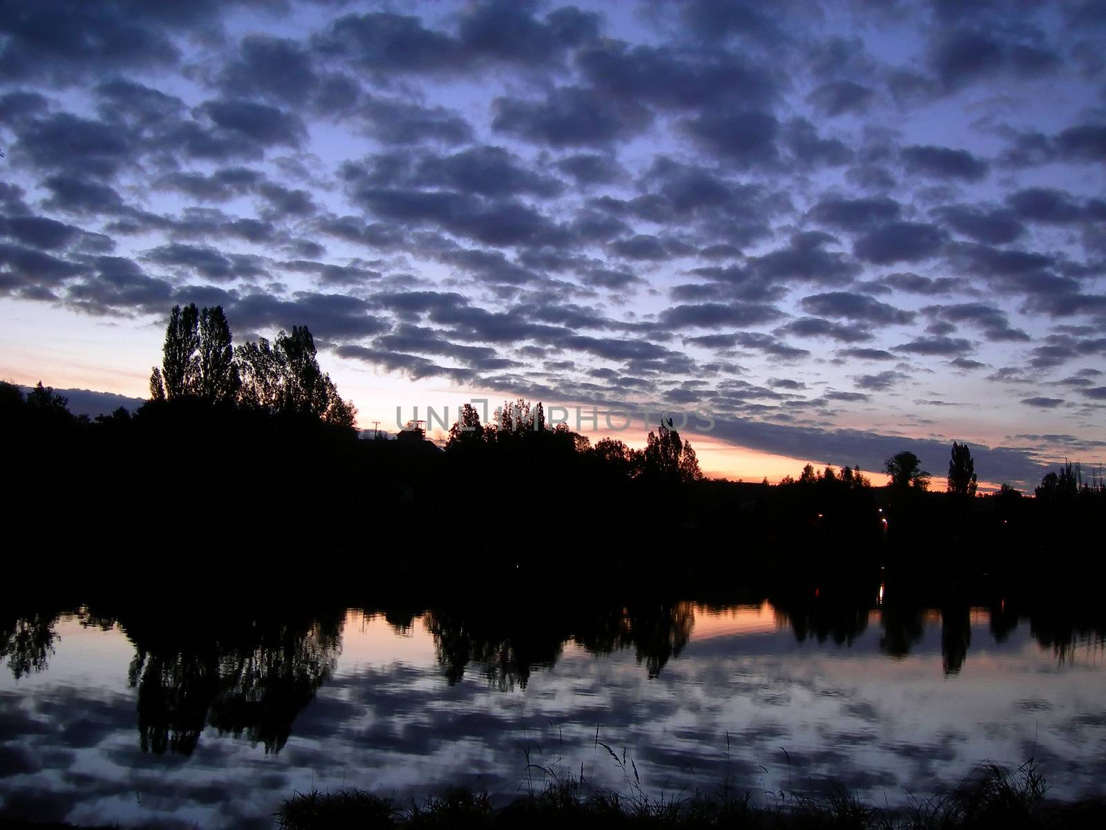           Beautiful sunset with clouds and lake with mirroring village