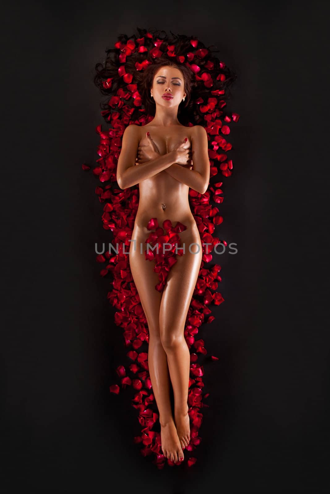 Beautiful woman against petals of red roses isolated on a black background