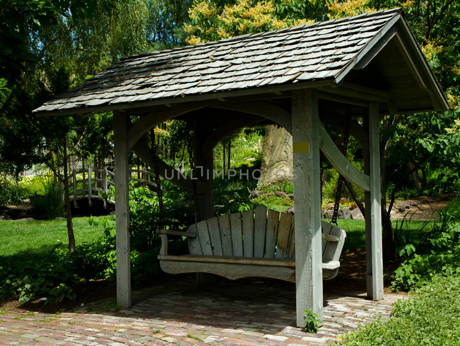 A relaxing wooden bench swing surrounded by green grass and trees