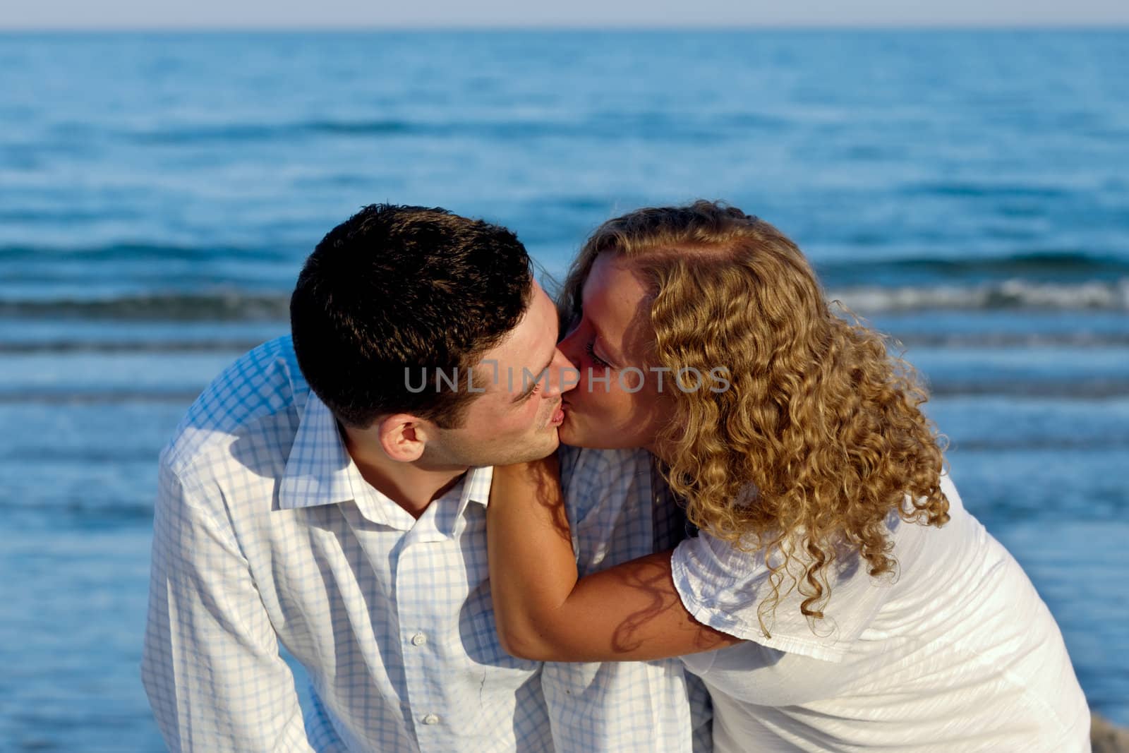 A young couple a standing near beach kissing.