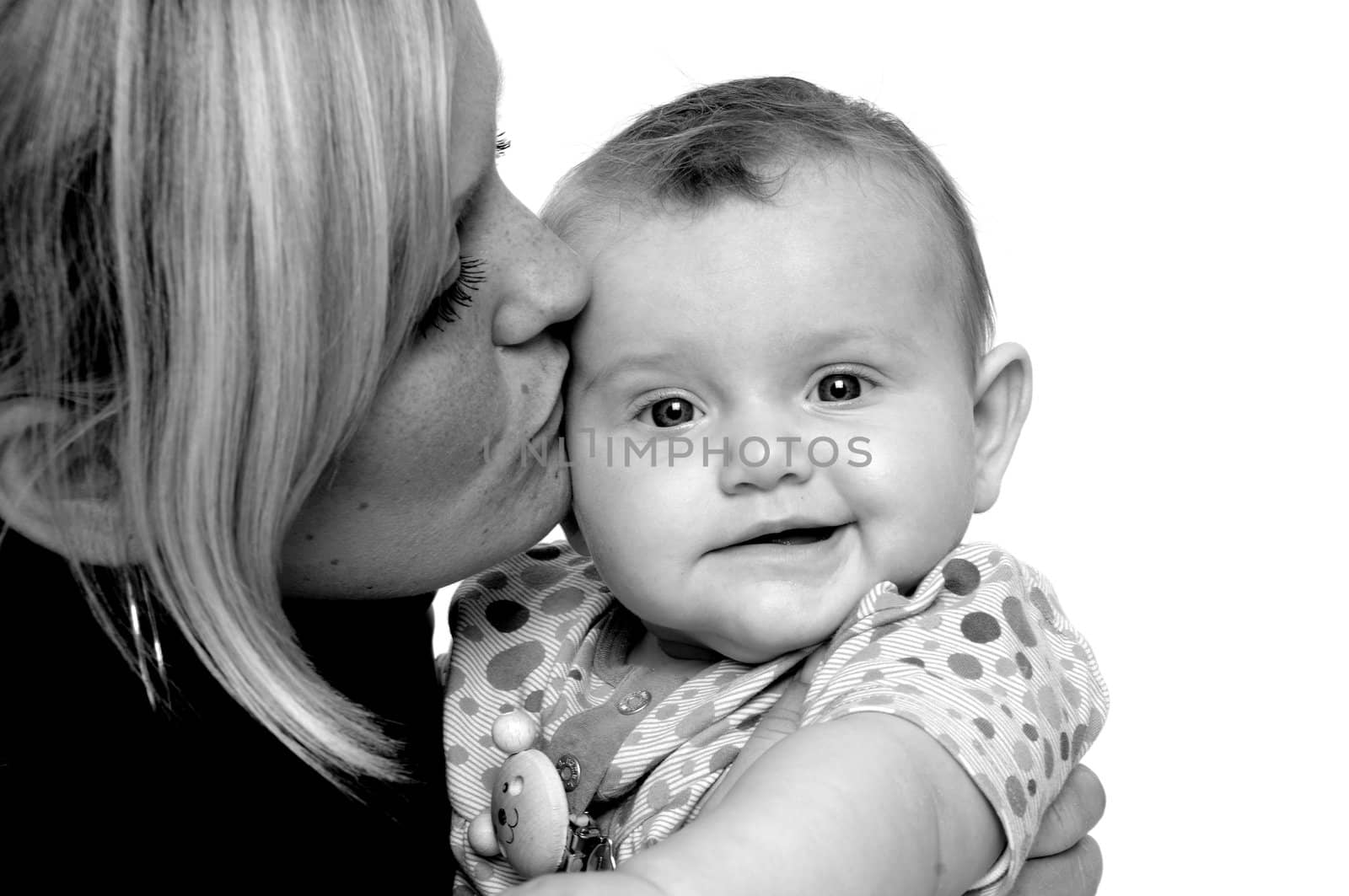 Mother is looking down on her sweet baby while kissing her. Taken on a white background.