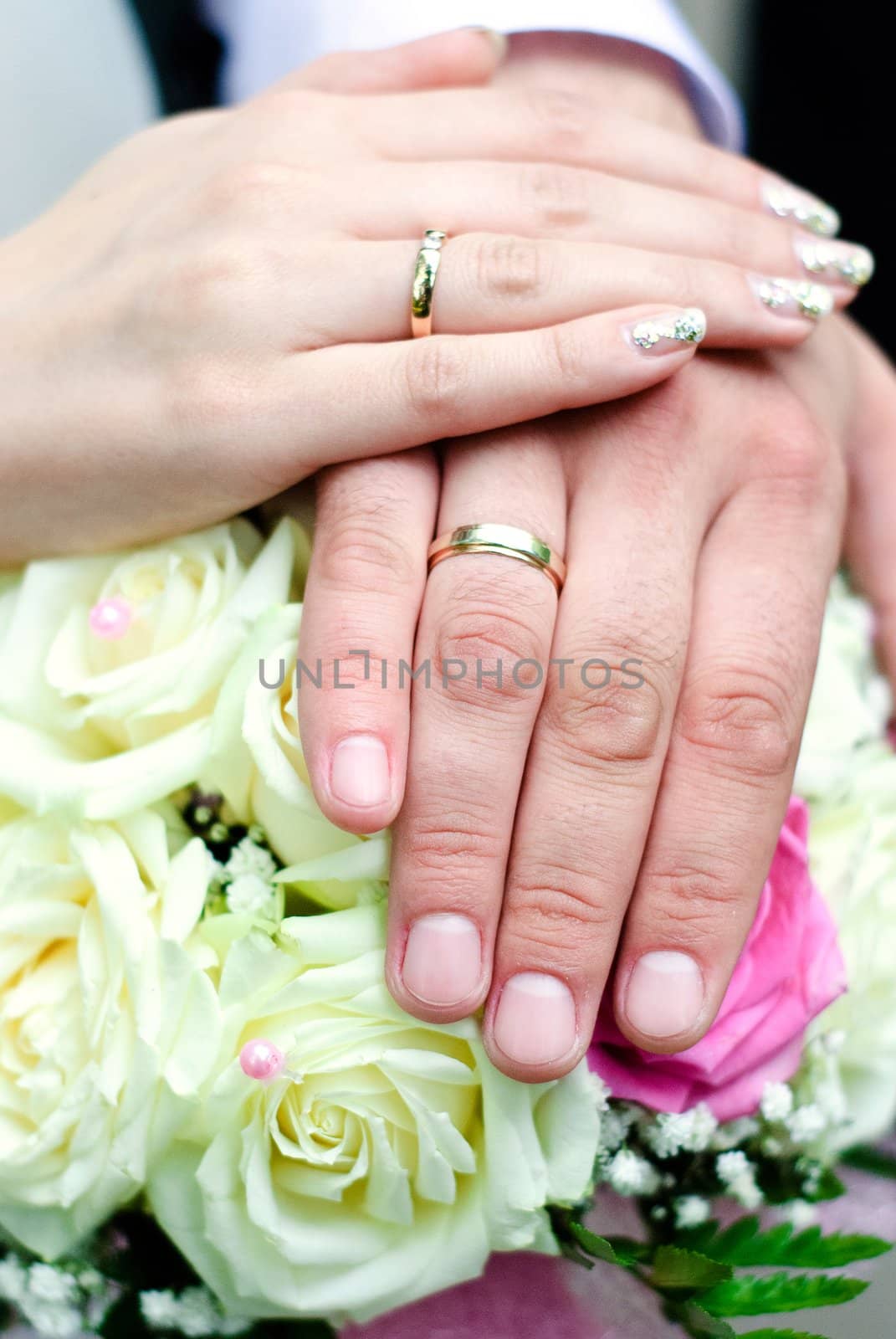 Hands of groom and bride with wedding rings on top of the bride's bouquet