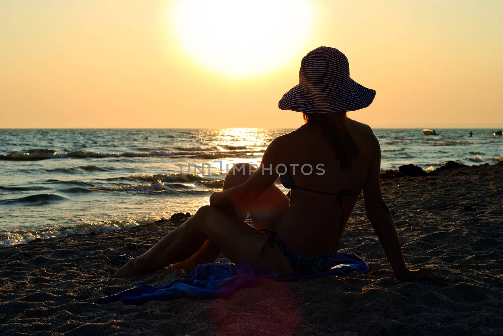 Young woman sitting on the beach at the sunset