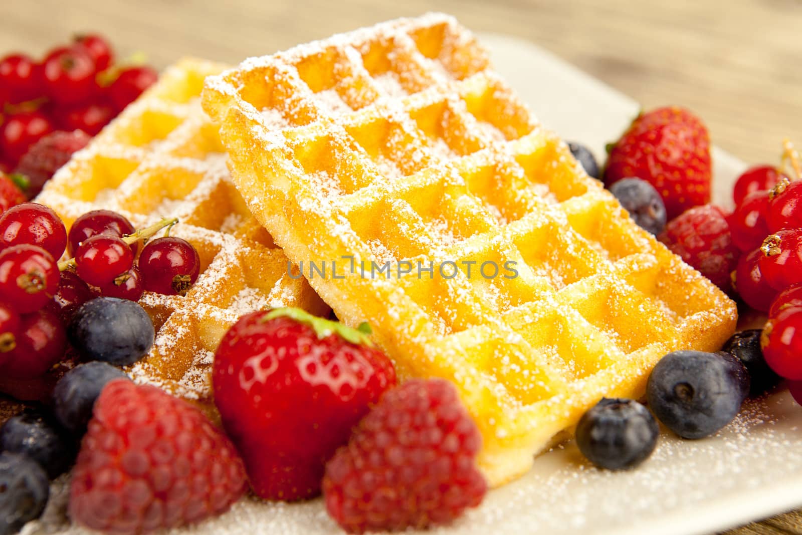 fresh tasty waffer with powder sugar and mixed fruits on wooden background