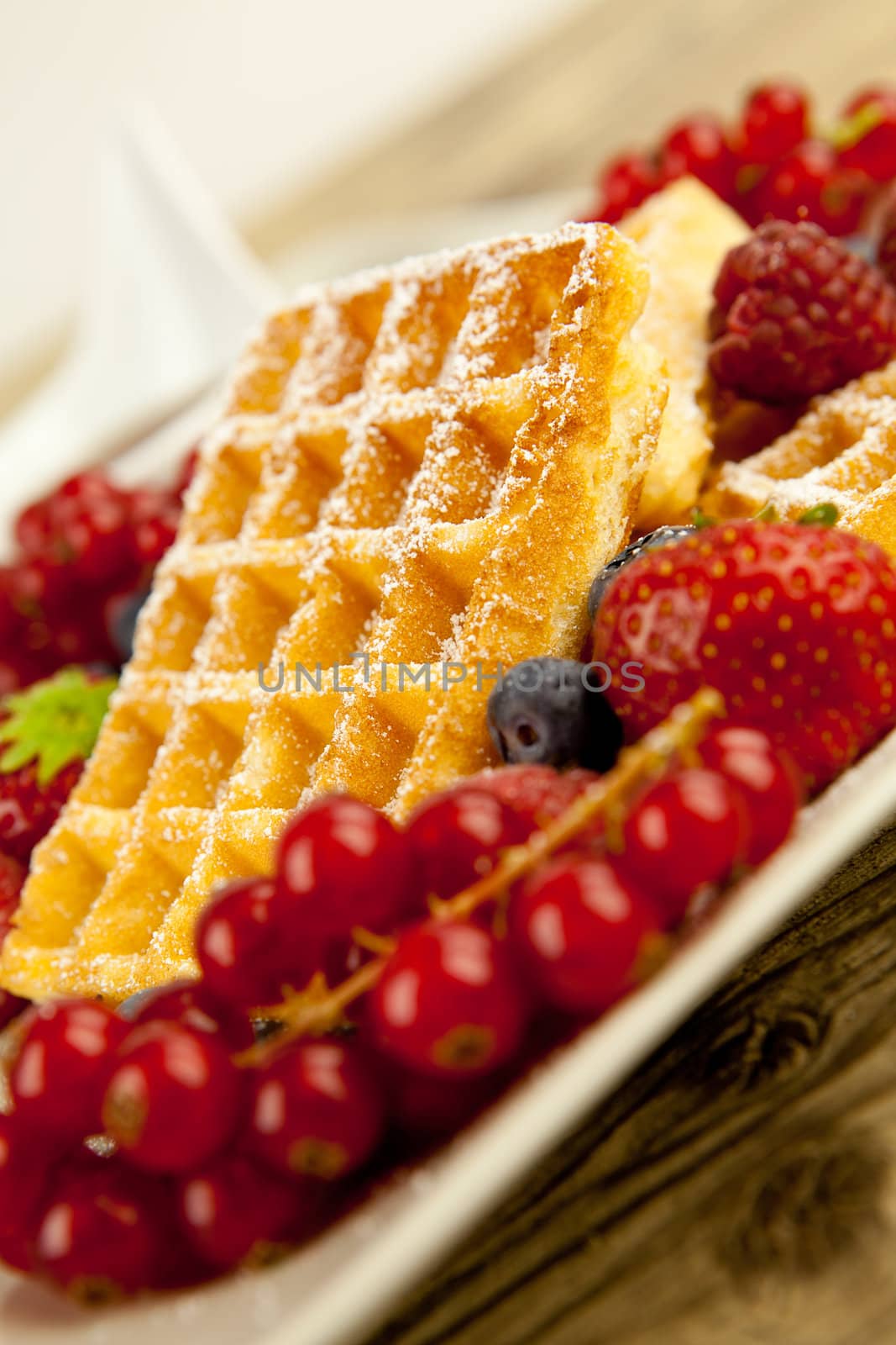 fresh tasty waffer with powder sugar and mixed fruits on wooden background