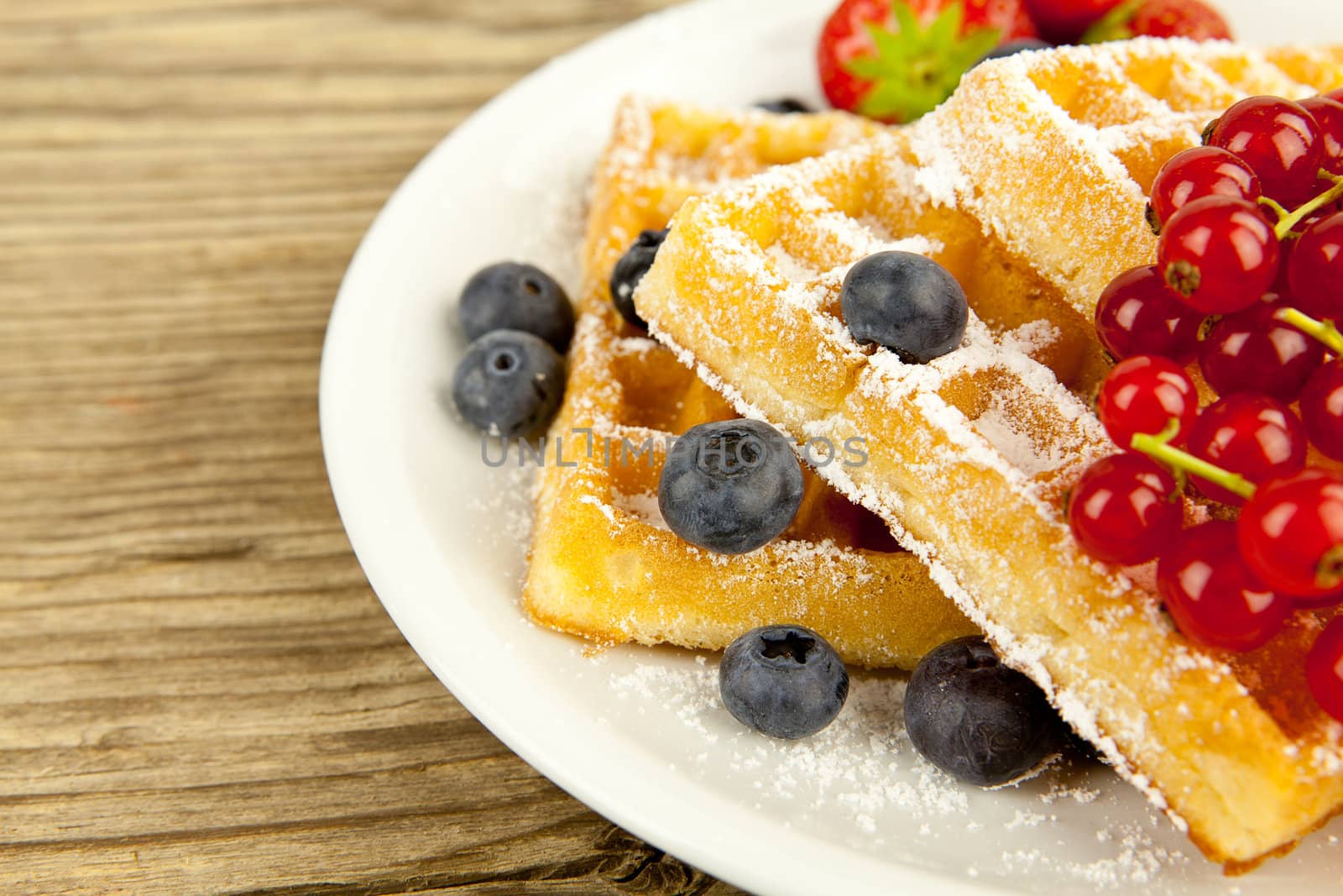 fresh tasty waffer with powder sugar and mixed fruits on wooden background