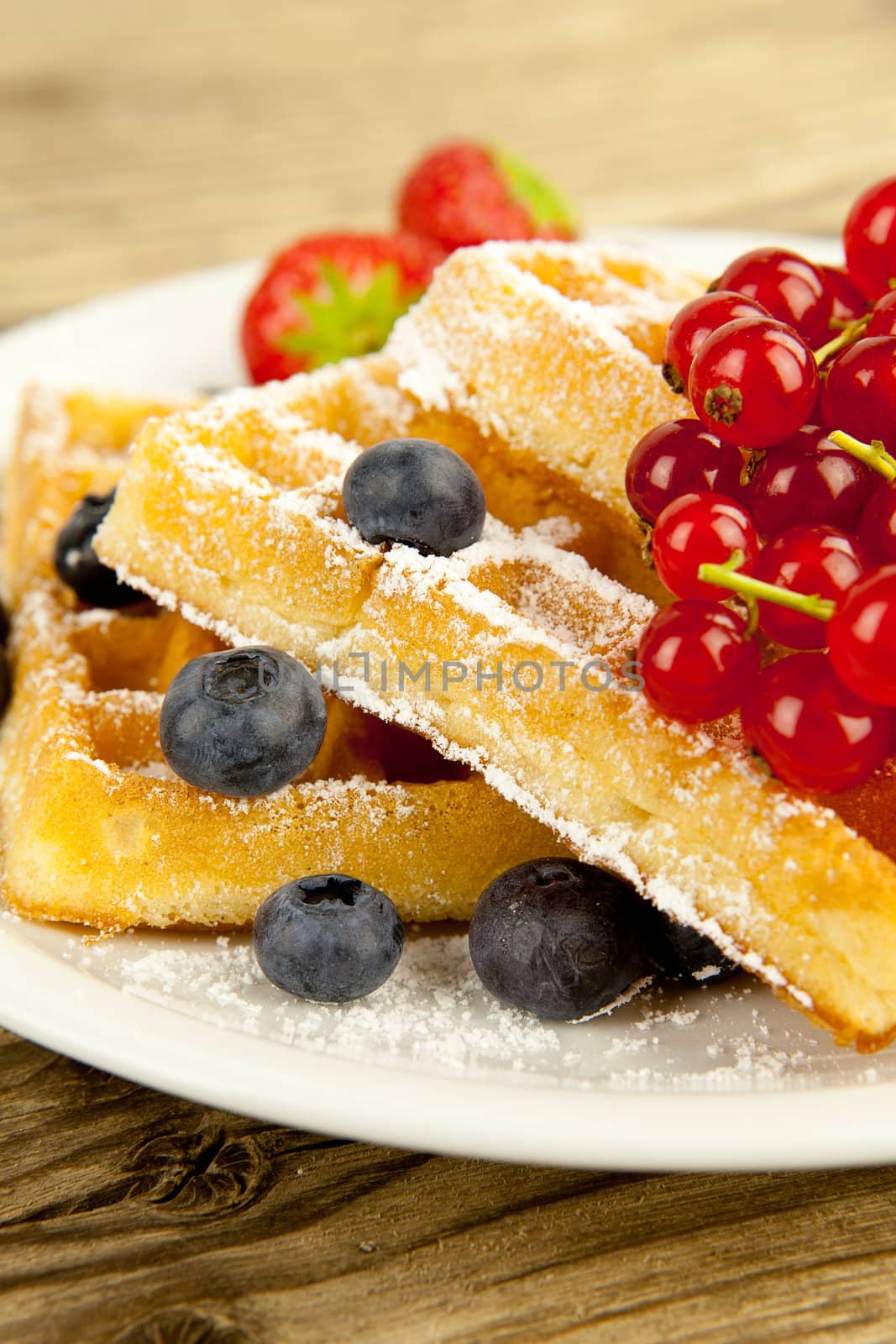 fresh tasty waffer with powder sugar and mixed fruits on wooden background