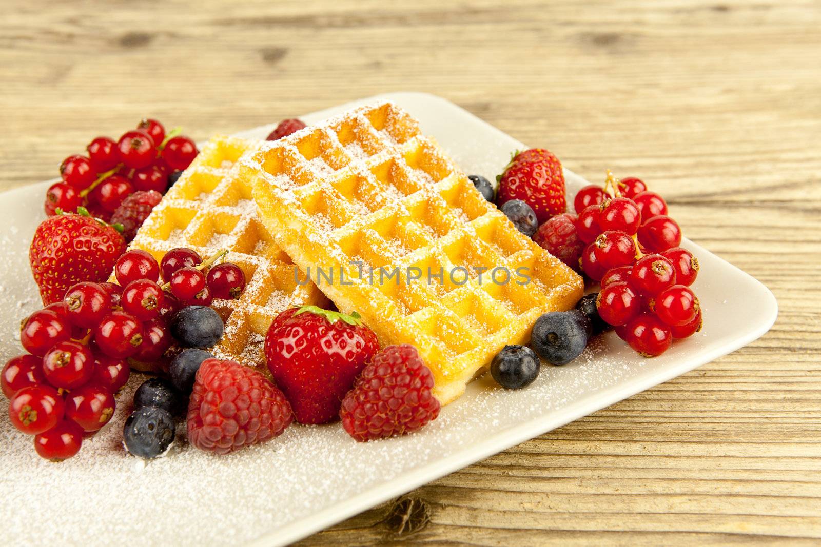 fresh tasty waffer with powder sugar and mixed fruits on wooden background