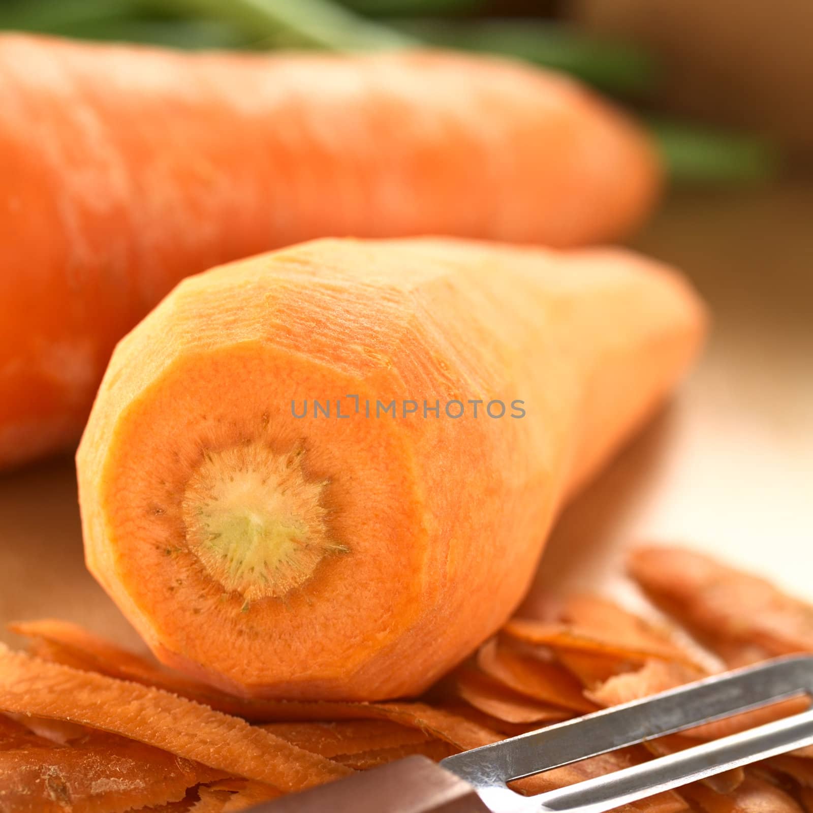 Raw peeled carrot with peeler on wooden board (Selective Focus, Focus on the front of the carrot)