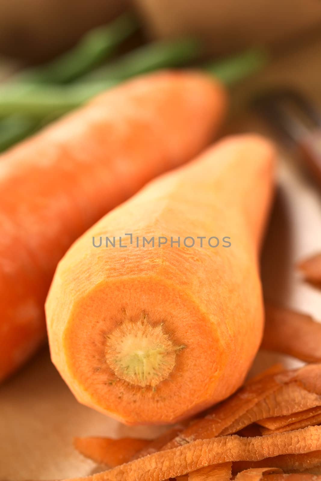 Raw peeled carrot with peel and other vegetables (green beans and potatoes) on wooden board (Selective Focus, Focus on the front upper edge of the carrot)