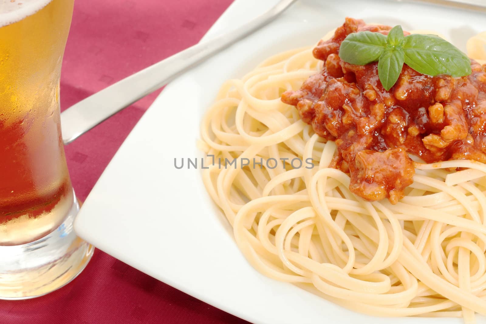 dish of noodles with tomato sauce and minced meat and beer glass in the foreground on a red background