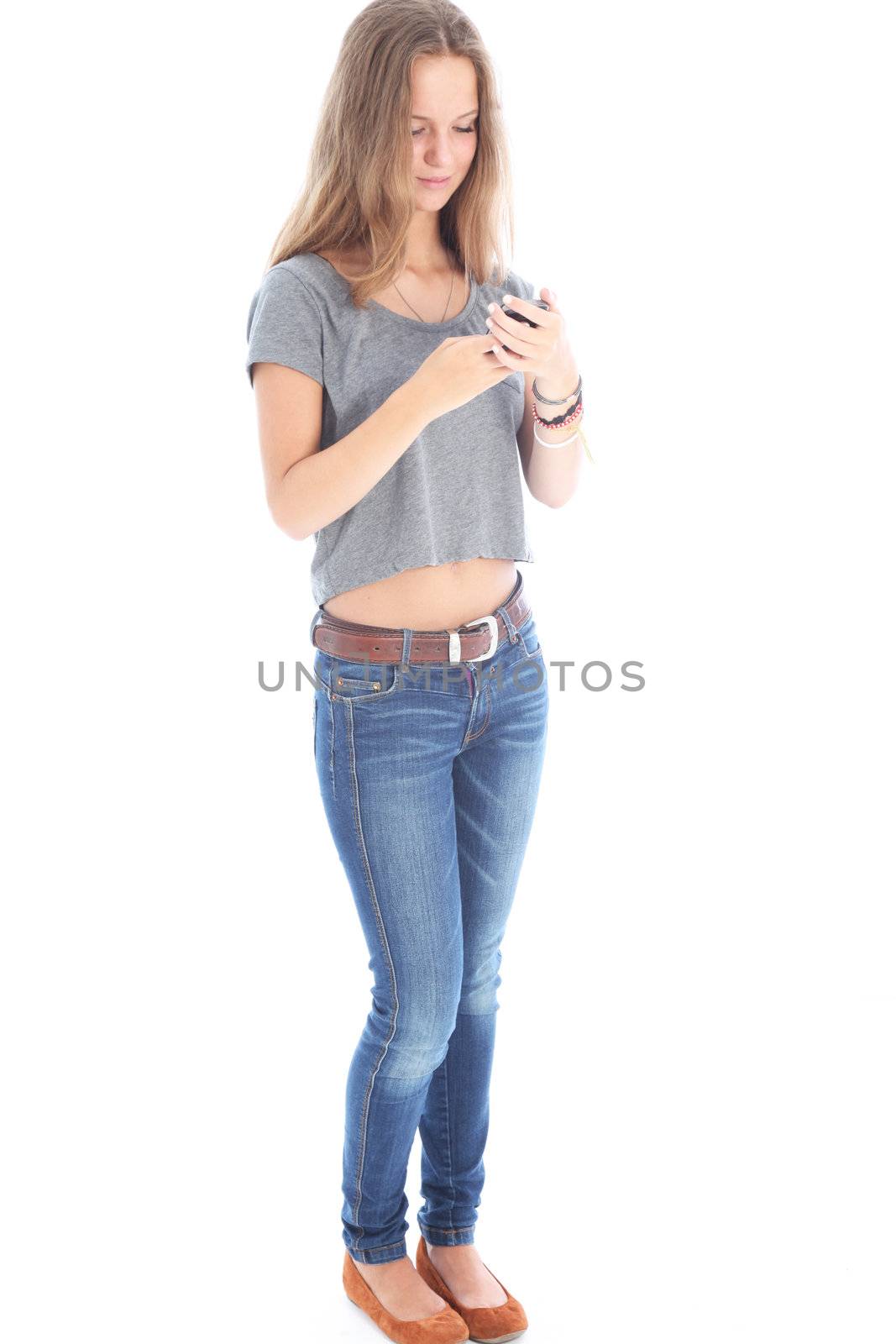 Slender young woman in jeans standing reading a text message on her mobile phone isolated on white 