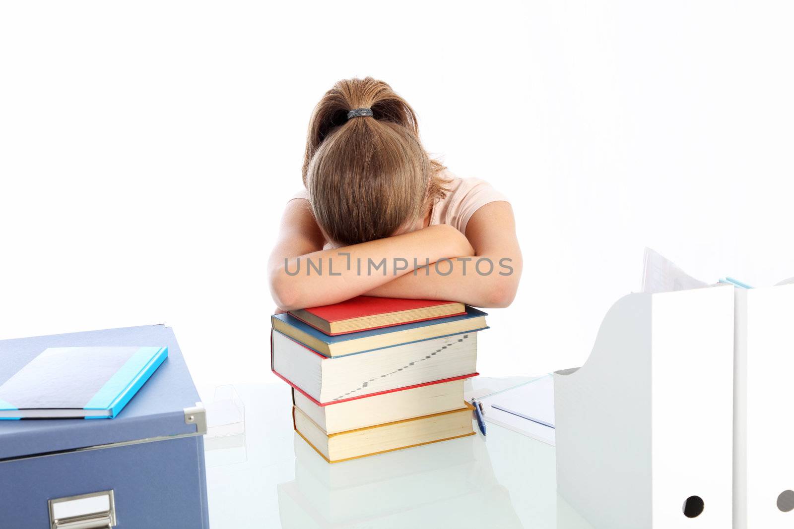 Young woman student seated at her desk asleep on a pile of books worn out by overwork and stress 