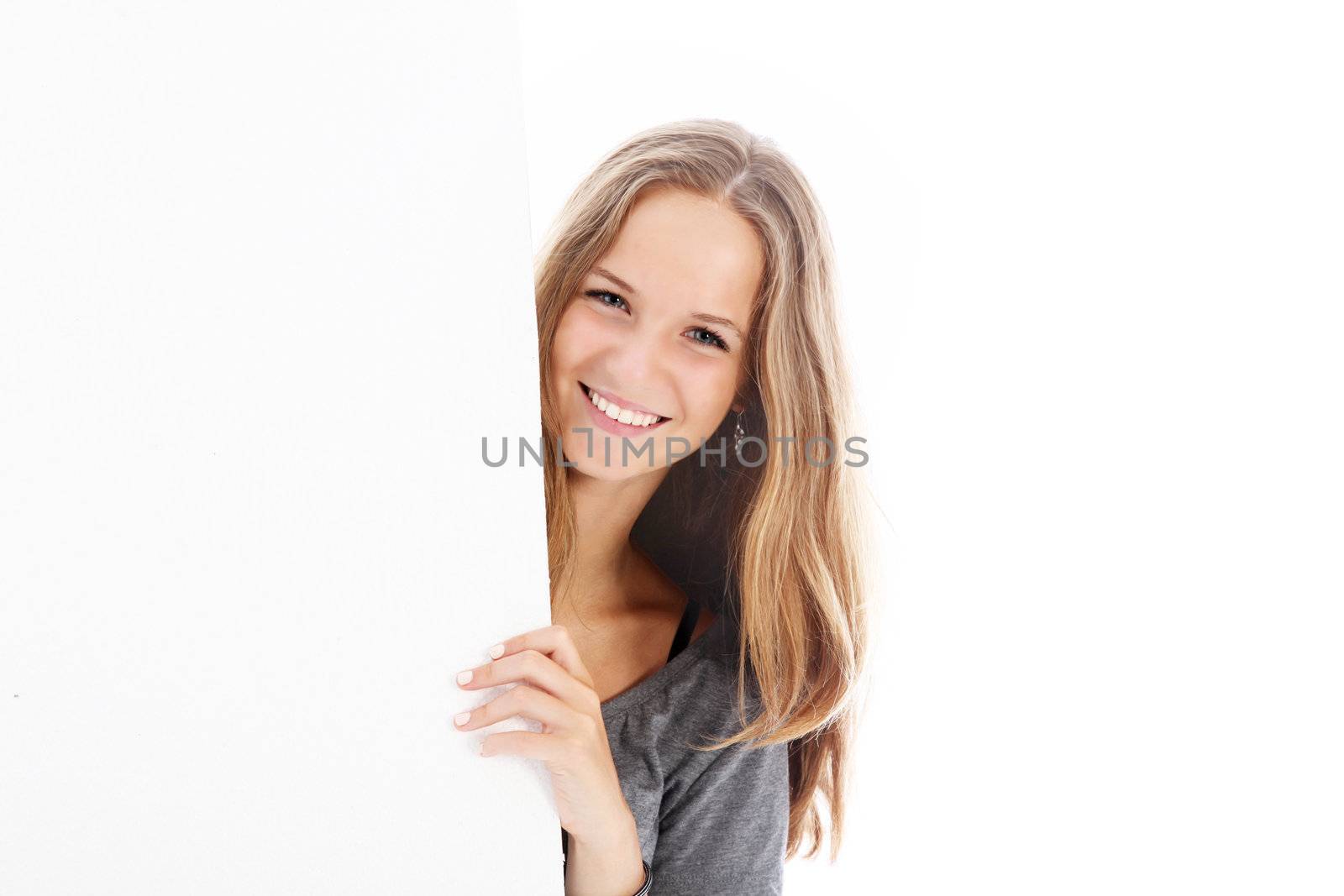 Smiling pretty young teenager standing alongside a blank white board for your text and advertising 
