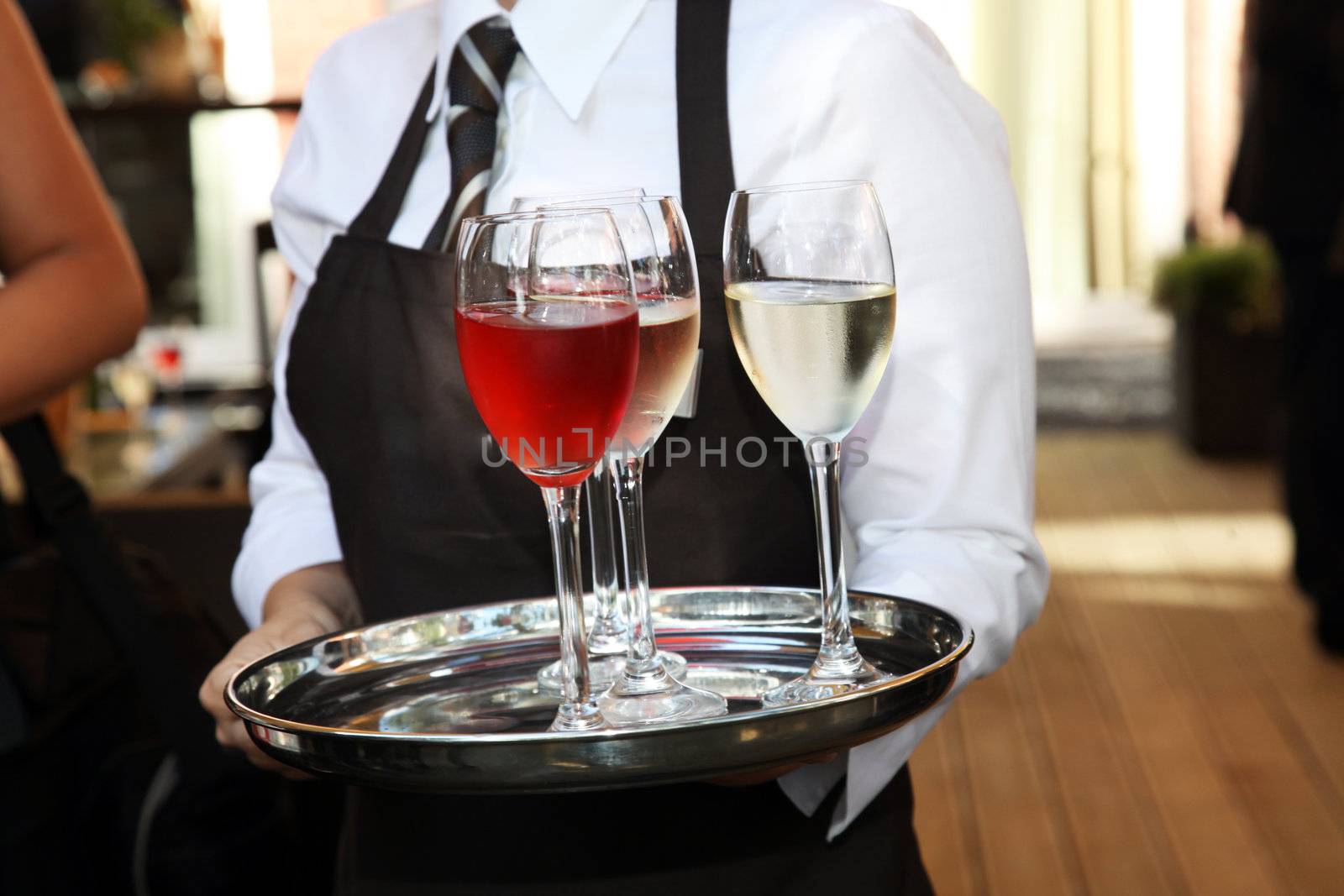 Cropped image of the torso of a waiter carrying wine glasses on a silver tray at a catered function 
