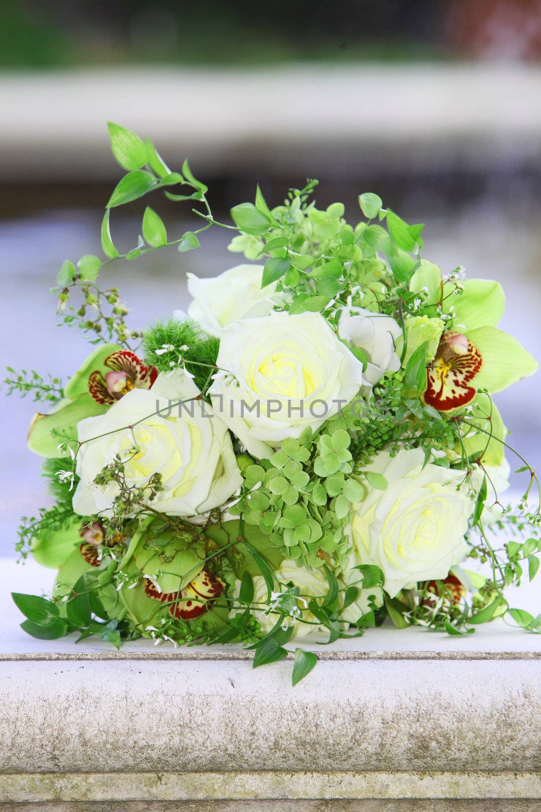 Pretty fresh floral bouquet with white roses, fresh foliage and green cymbidium orchids lying on a stone parapet outdoors 
