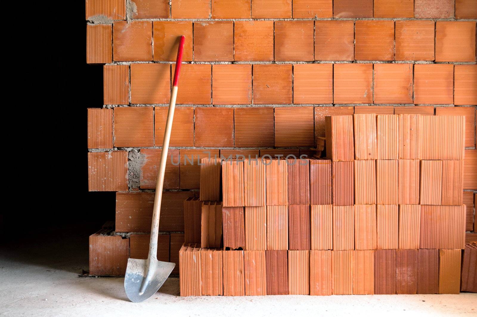 Brick wall with shovel, bucket and many bricks in a under construction masonry site.