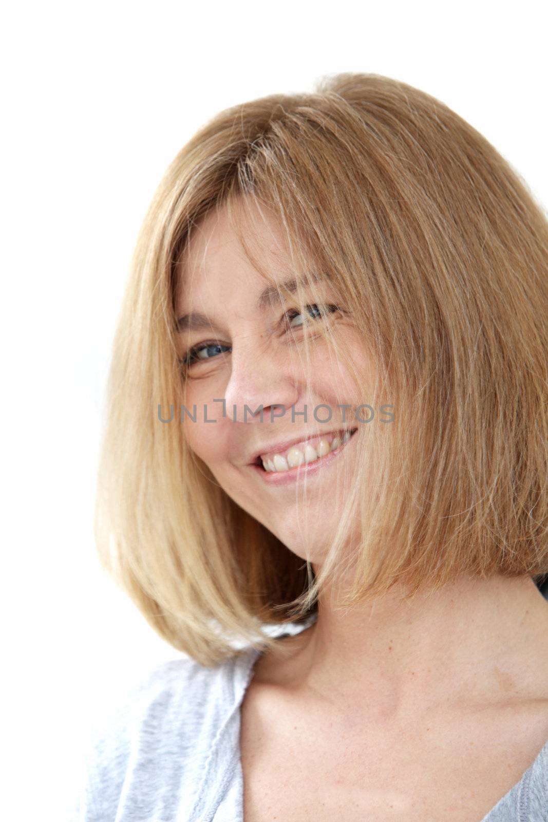 Happy blonde woman with a lovely wide toothy smile standing sideways looking at the viewer, headshot on white