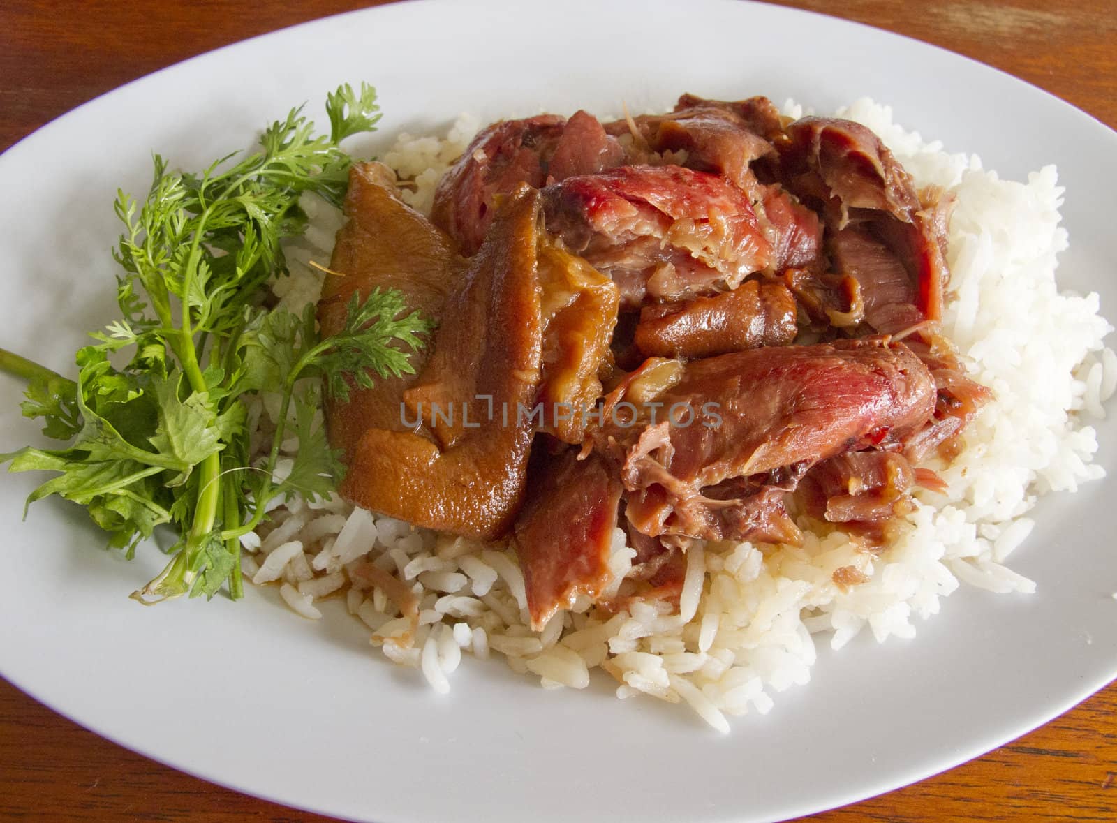 Thai stewed pork leg with rice and parsley (Kao Ka Moo) on white plate