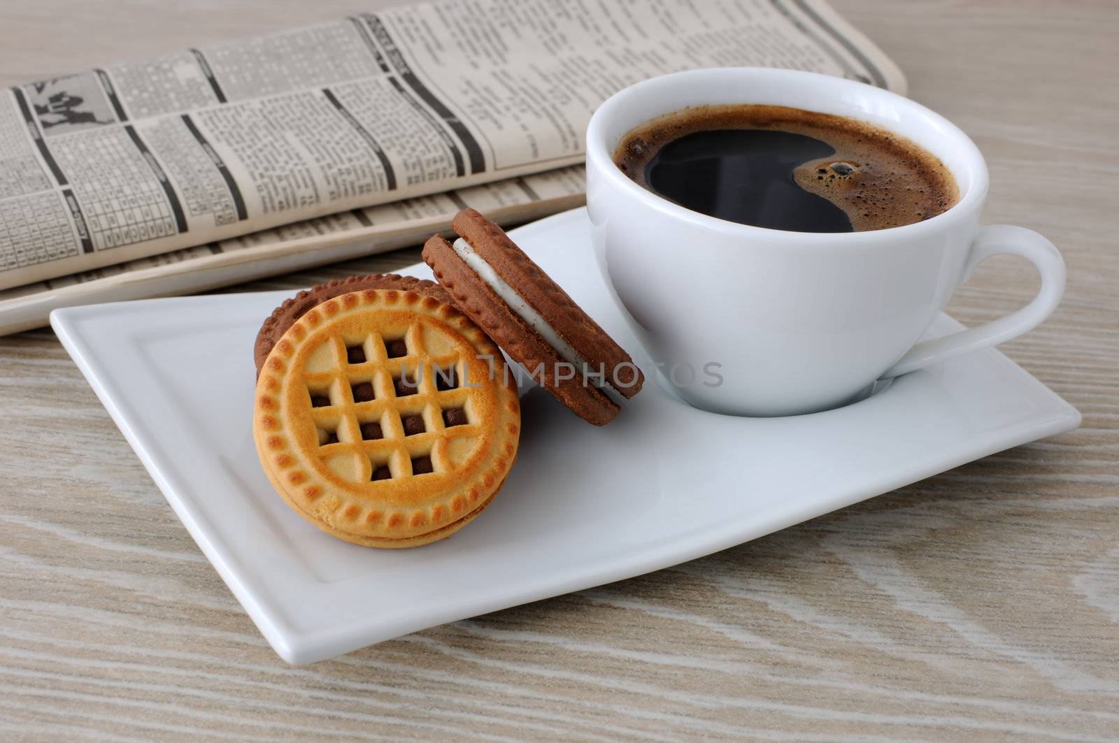 A cup of fresh brewed coffee and biscuits on the table with newspaper