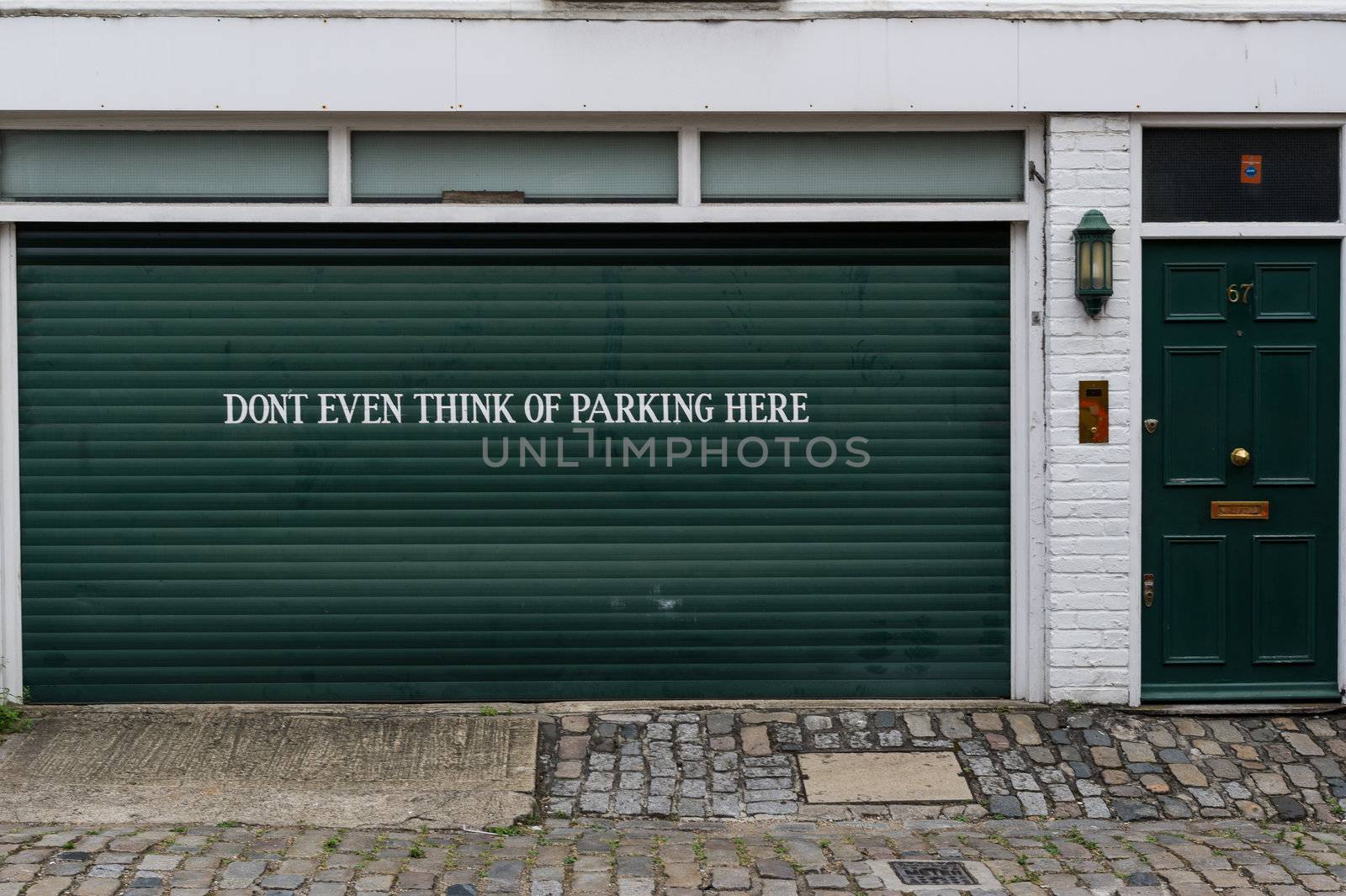 Garage sign prohibiting parking painted on the door of a private garage saying "Dont even think of parking here"