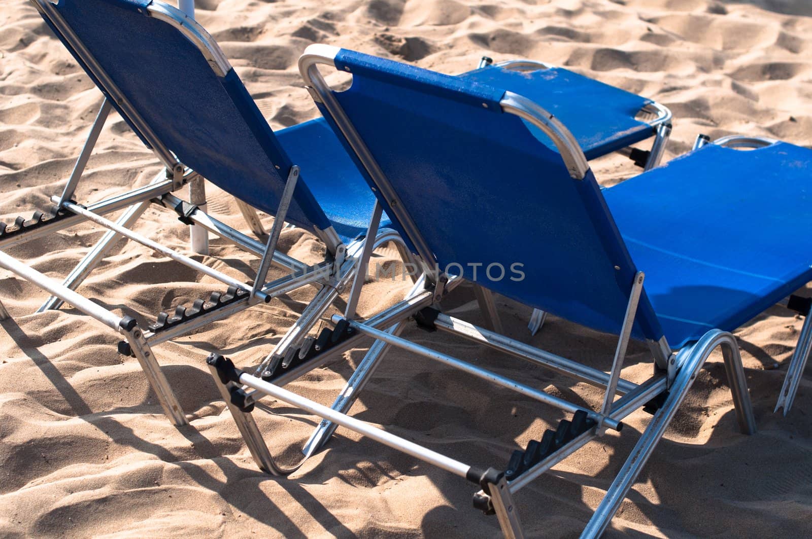 2 lonely blue sunbeds on sandy beach
