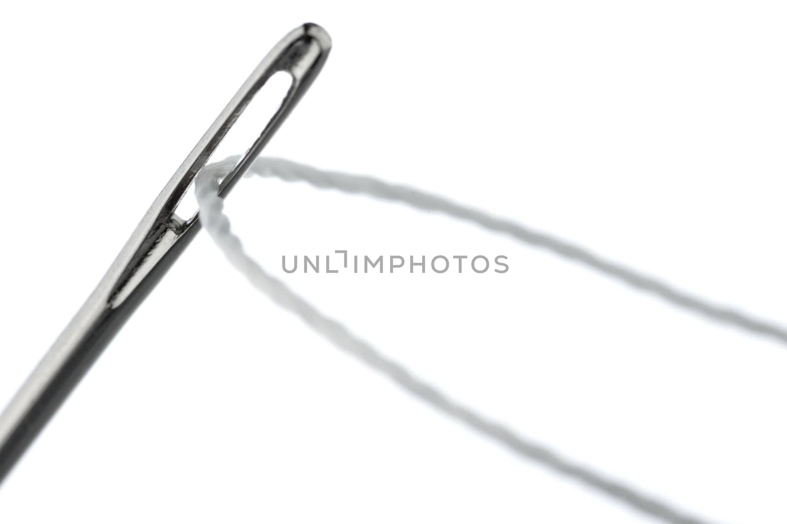 Thread inserted through the needle's eye, photographed on a white background