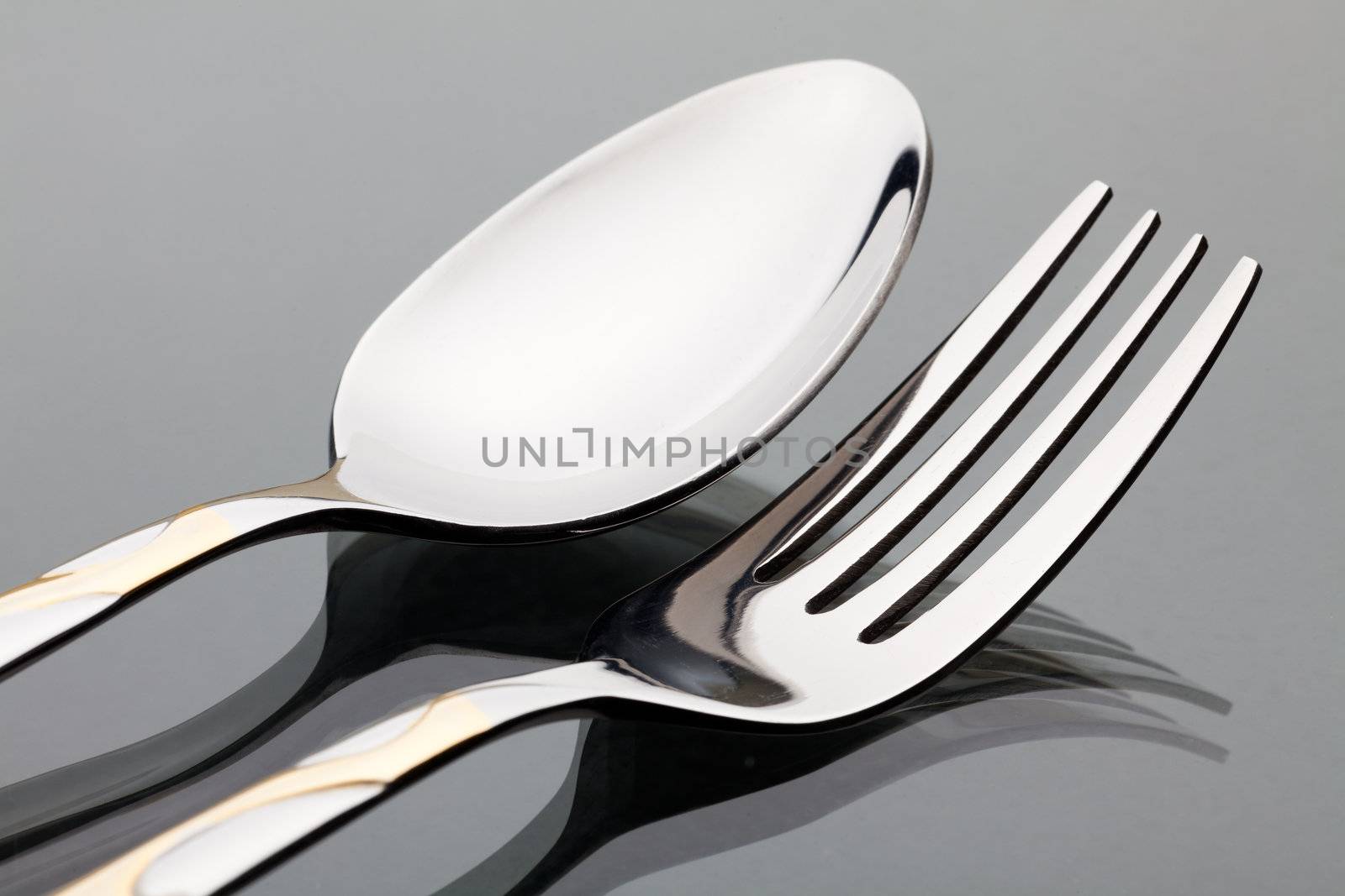 Spoon and fork are on the glass desk. Close-up