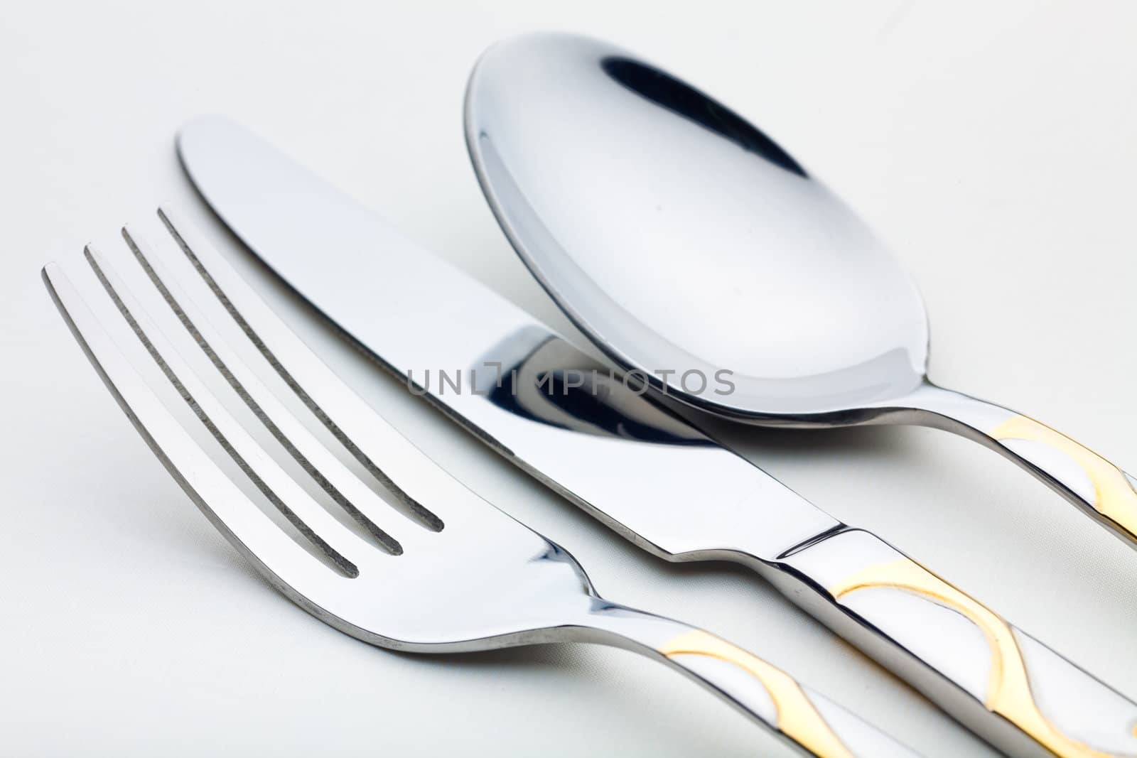 Chrome-plated spoon, a knife and fork are on the white tablecloth. Frame close-ups