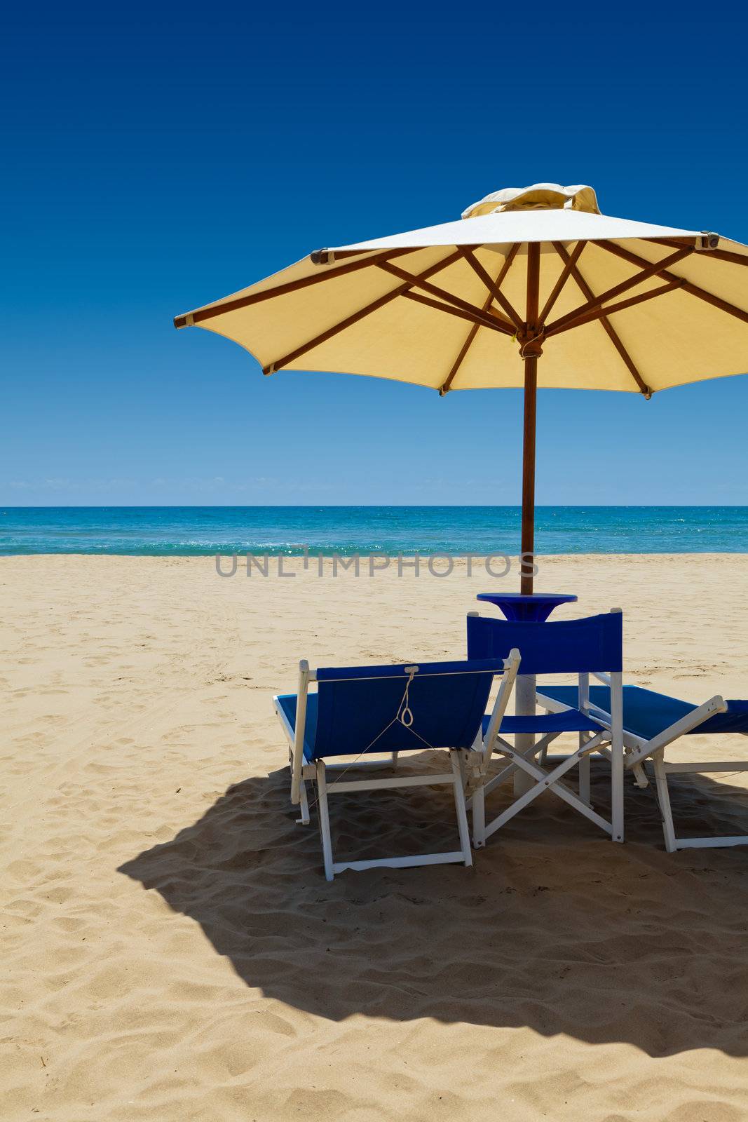 Deck chairs under an umbrella in the sand against the blue sea