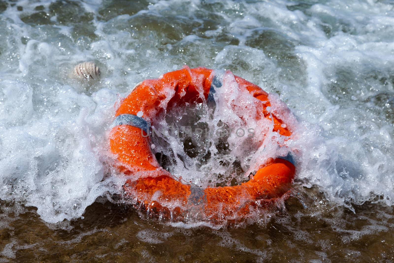 Red lifebuoy lies on the sand on the beach in foamy waves