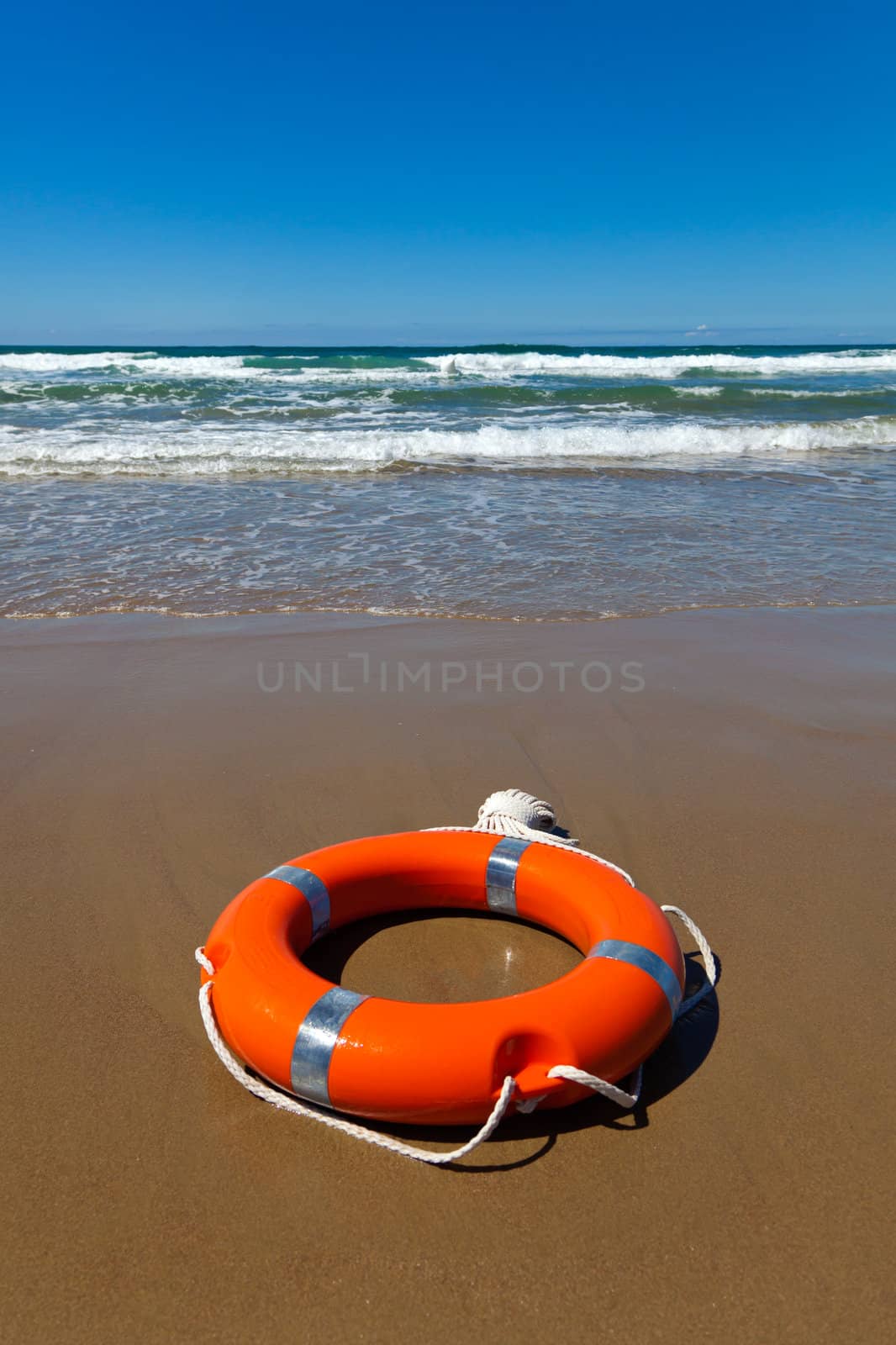 Red lifebuoy with a rope lying on the sand against the background of the southern sea on a sunny day