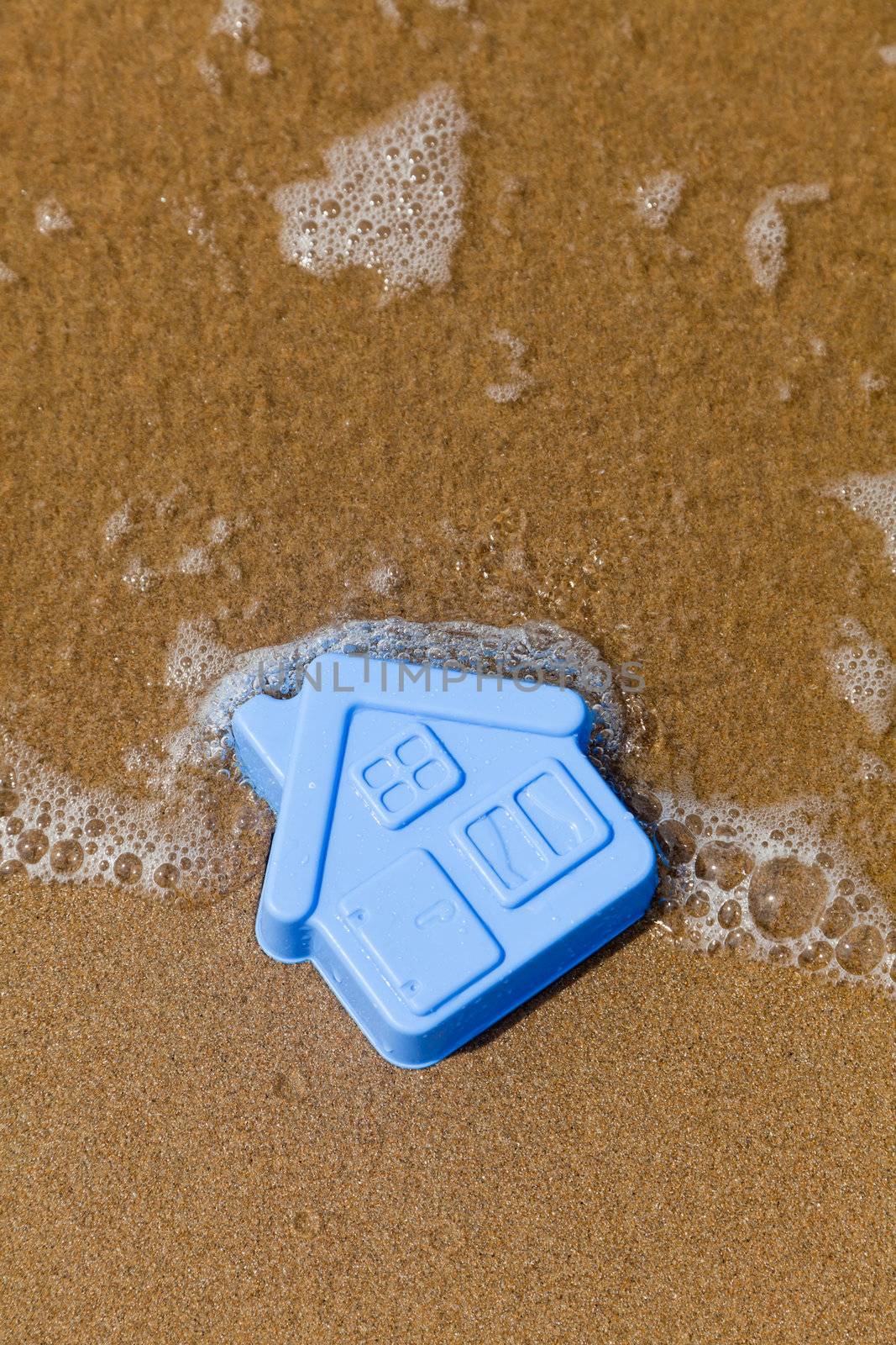 Blue toy plastic house on the sand washes wave