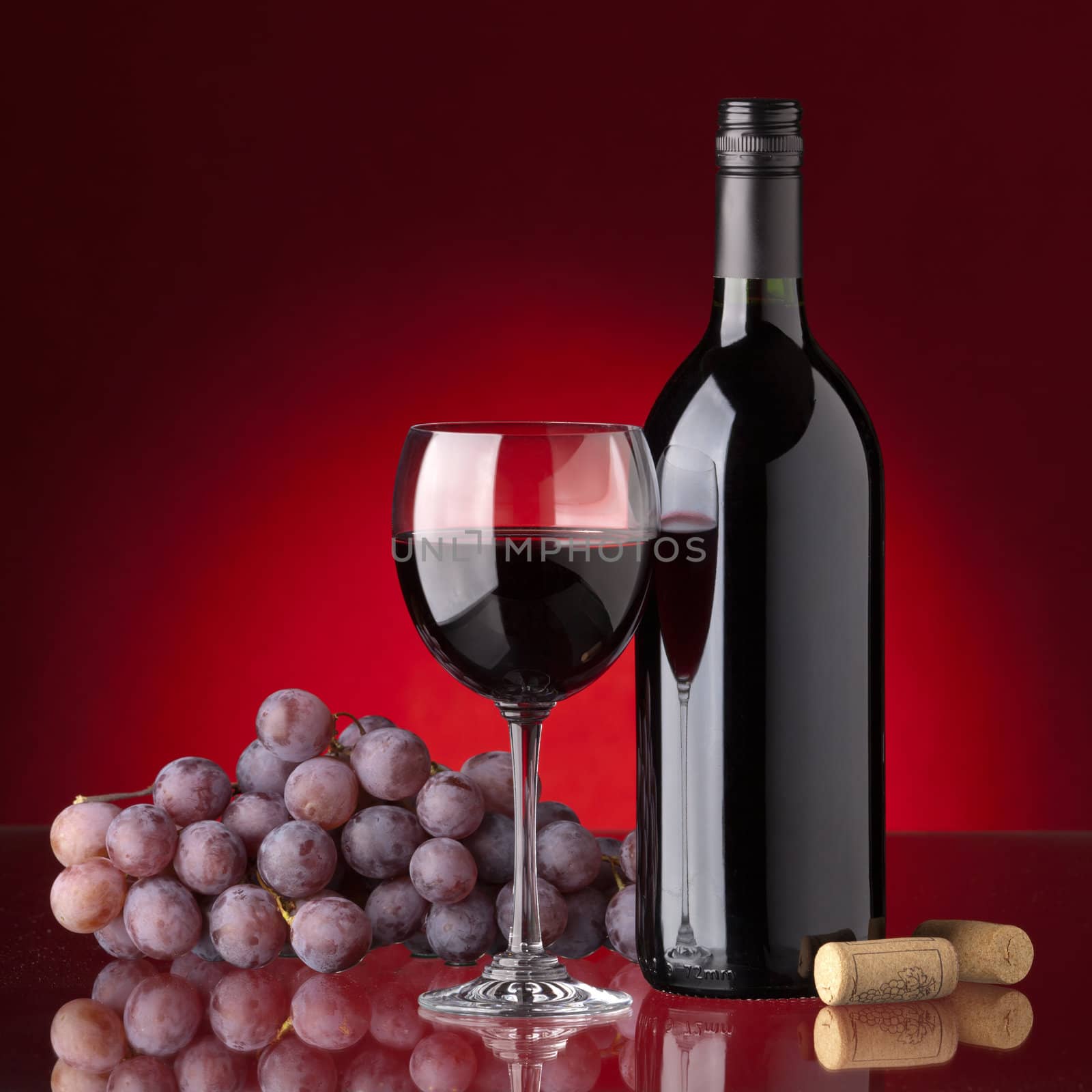Bottle and glass of red wine, grape and cork on a red background