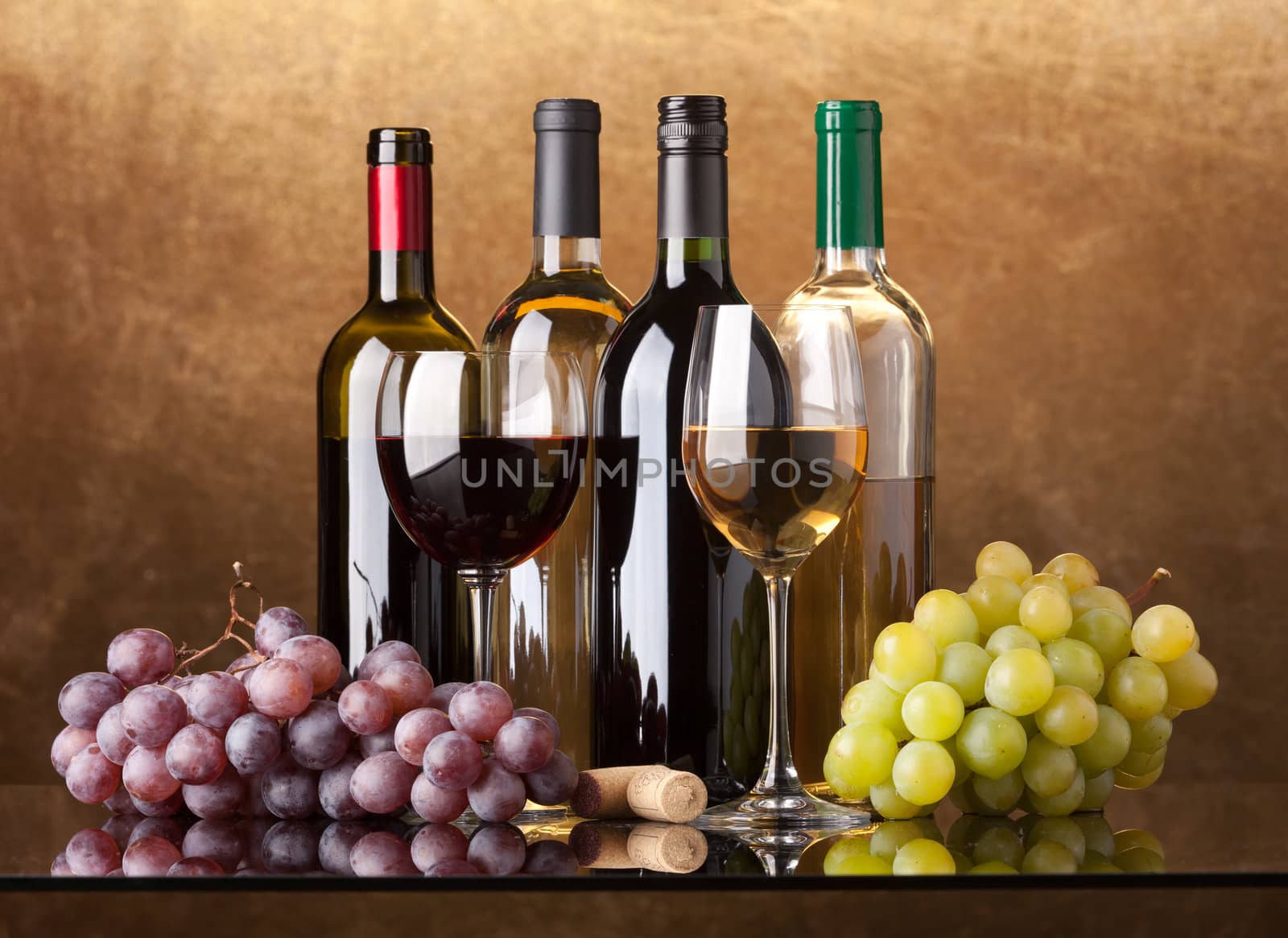 Several bottles of white and red wine, two glasses and grapes on a golden background