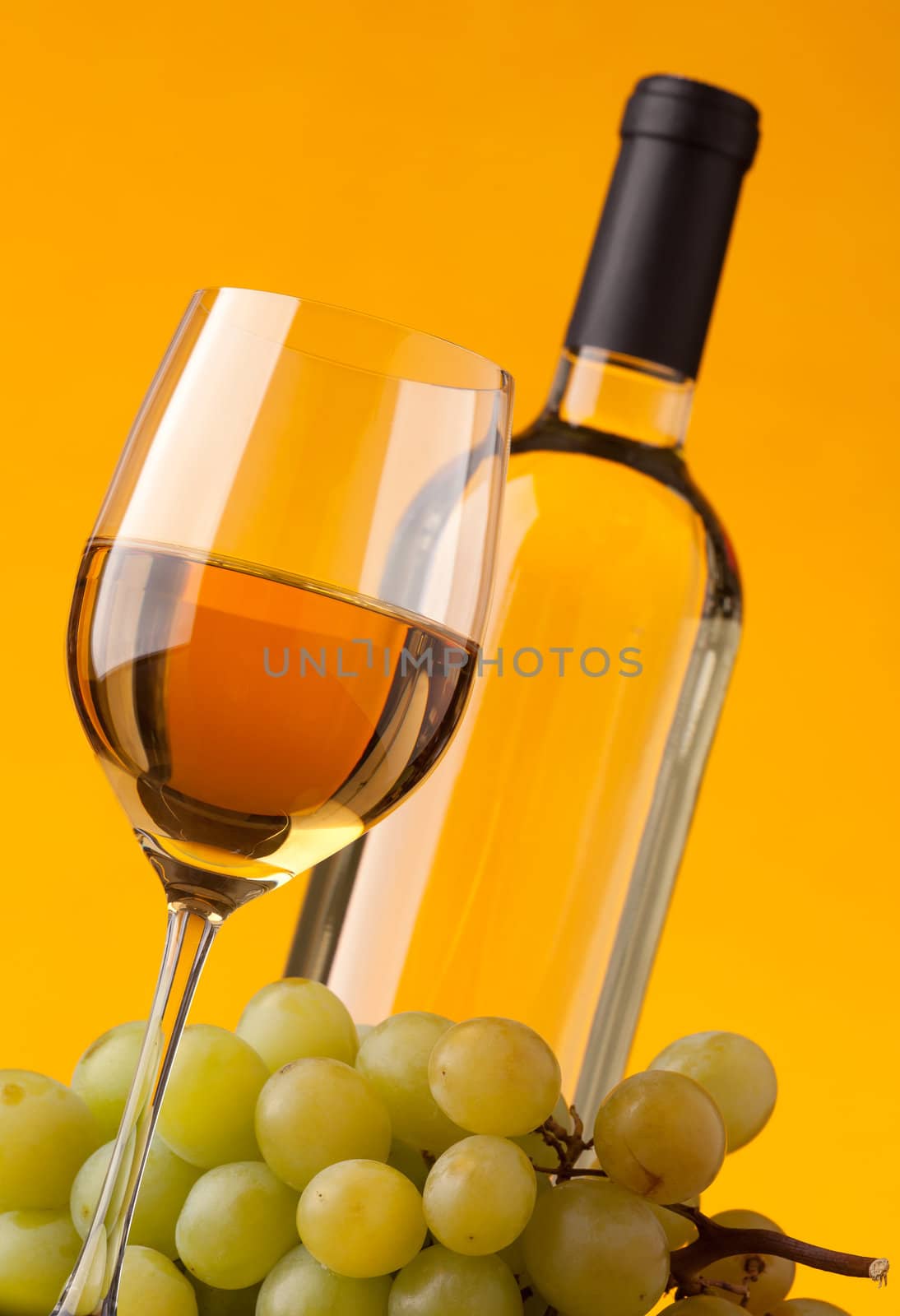 Bottom view of a glass of white wine bottle and grapes on a yellow background