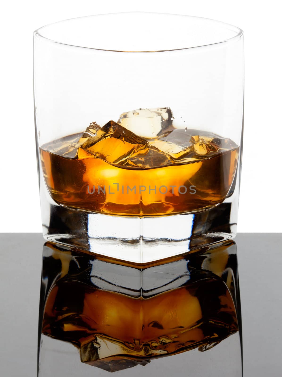 Glass of whiskey with ice cubes on a black reflective glass and white background