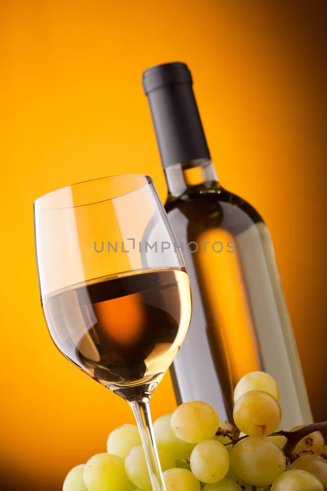 Bottom view of a glass of white wine bottle and grapes on a yellow background