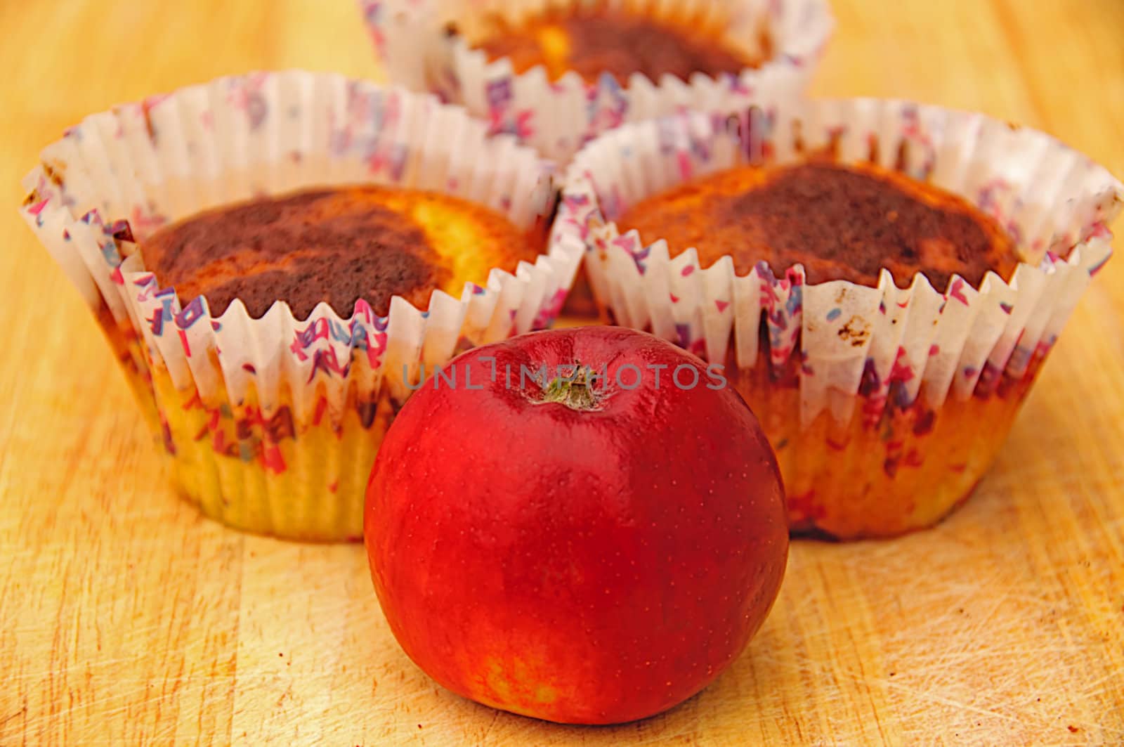 Three apple muffins and a red apple in front